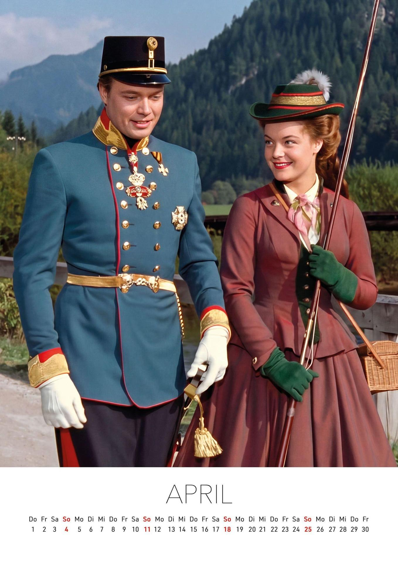 Ein Mann in Militäruniform und eine Frau in Vintage-Kleid spazieren im Freien vor Bergkulisse.