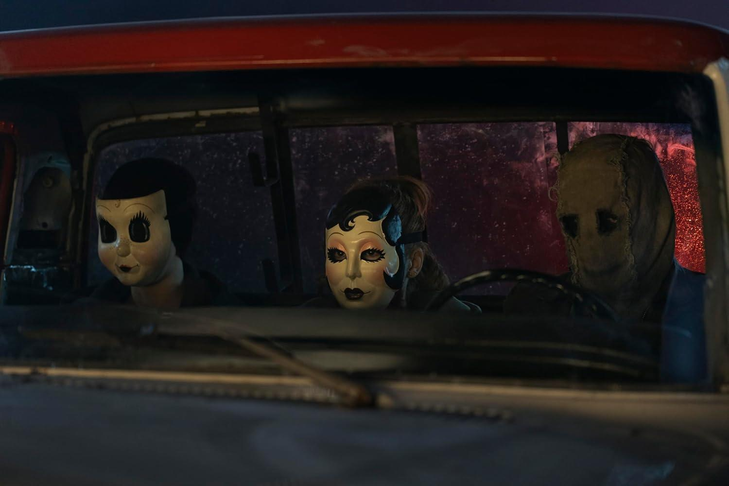Drei Personen mit gruseligen Masken sitzen im dunkeln Inneren eines roten Autos.