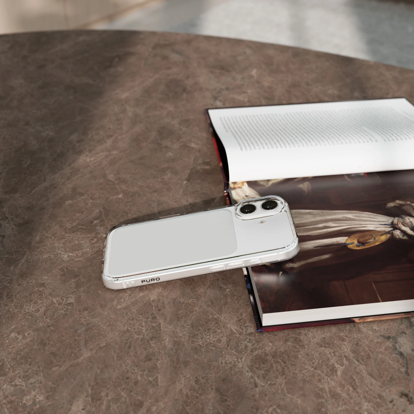 Ein weißes Smartphone in einer klaren Hülle liegt neben einem offenen Buch auf einem Marmortisch.