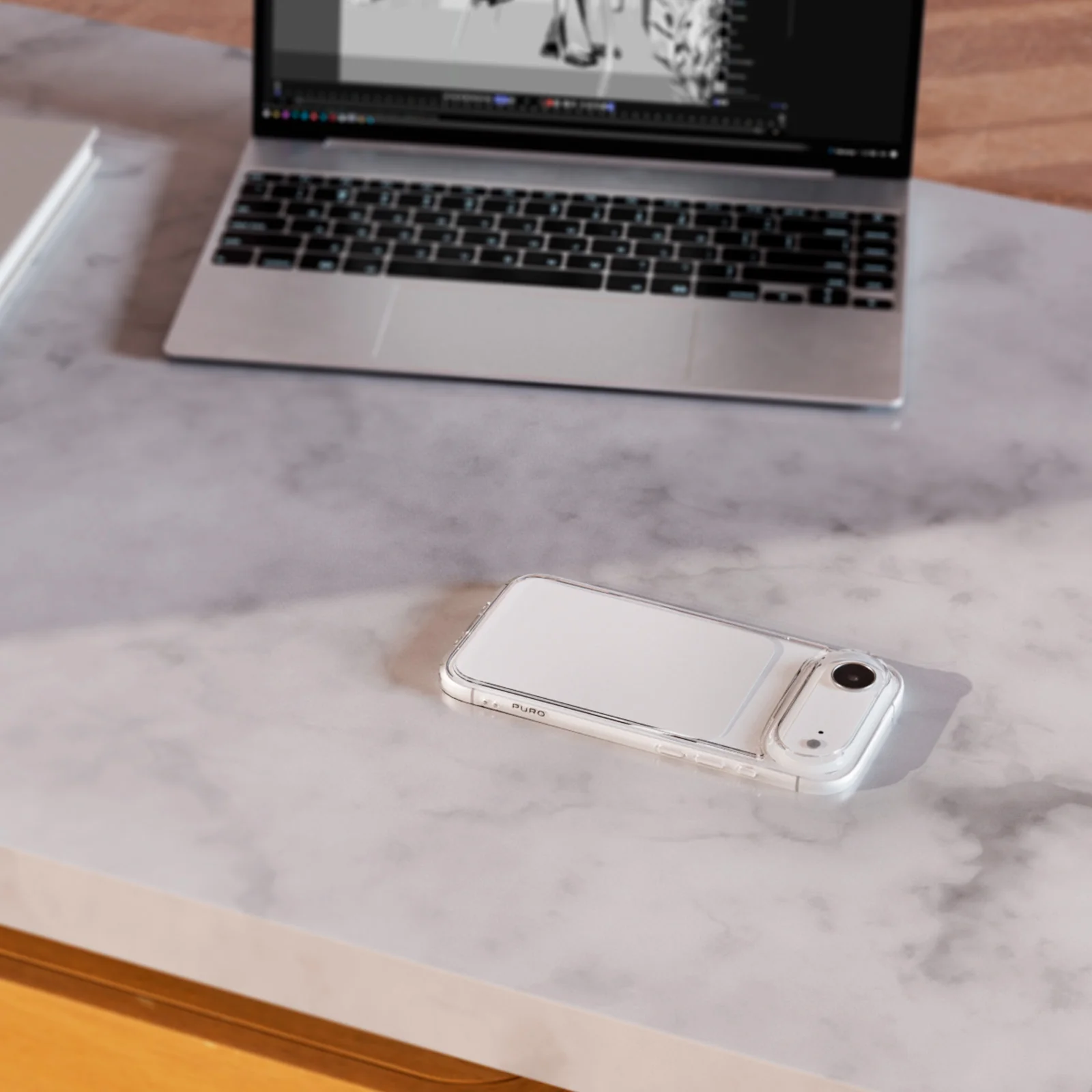 Ein Smartphone in einer transparenten Hülle und ein Laptop liegen auf einem Marmortisch.