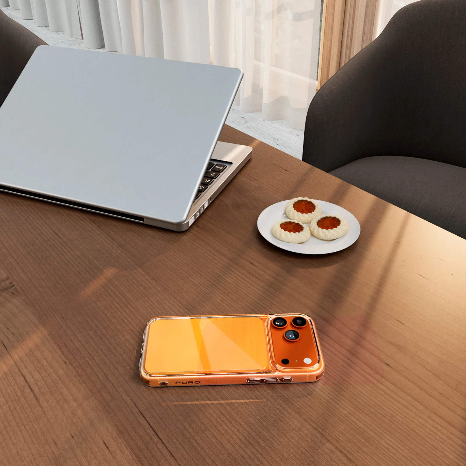 Ein Holztisch mit einem Laptop, einem Teller mit drei Keksen und einem orangefarbenen Smartphone in einer transparenten Hülle.