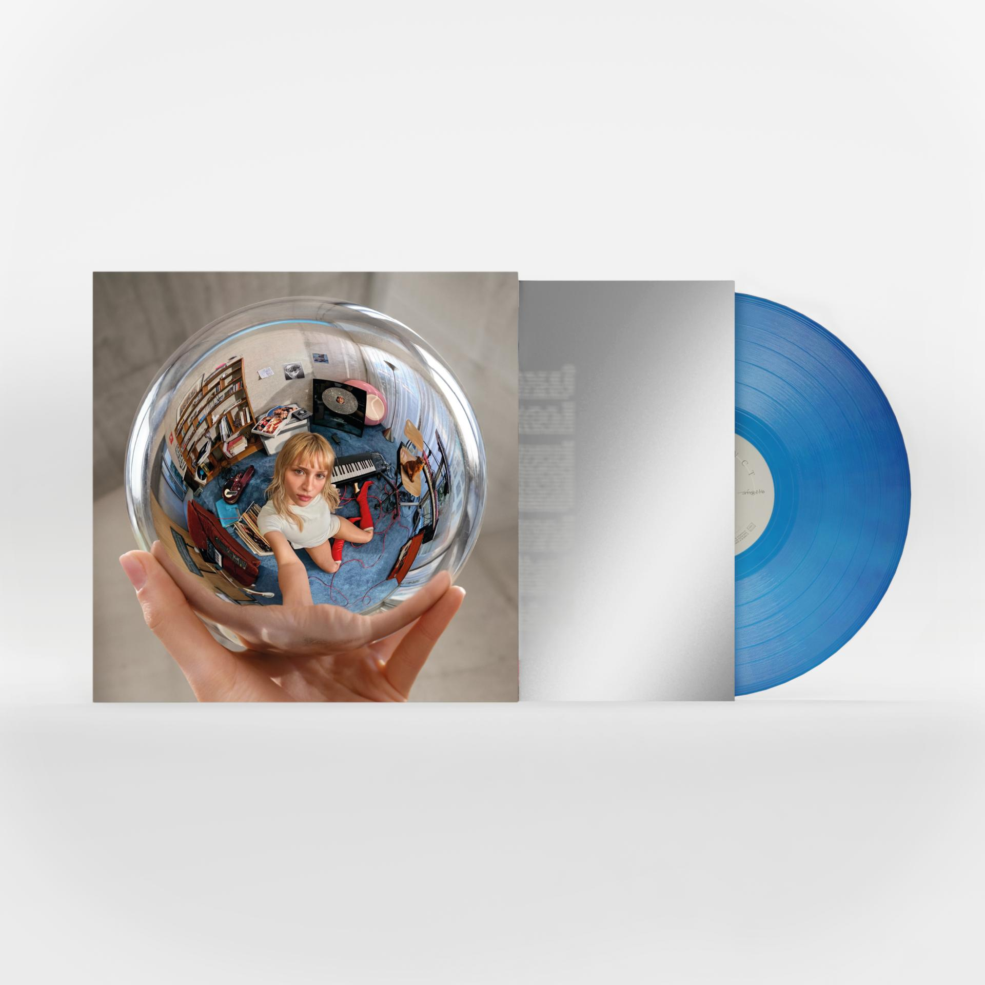Eine Hand hält eine Glaskugel mit einem Raumspiegelbild; daneben eine silberne Hülle und eine blaue Vinylplatte.