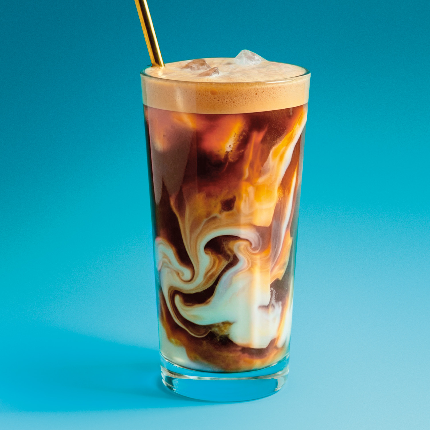 Ein Glas Eiskaffee mit milchigen Wirbeln und einem goldenen Strohhalm vor blauem Hintergrund.