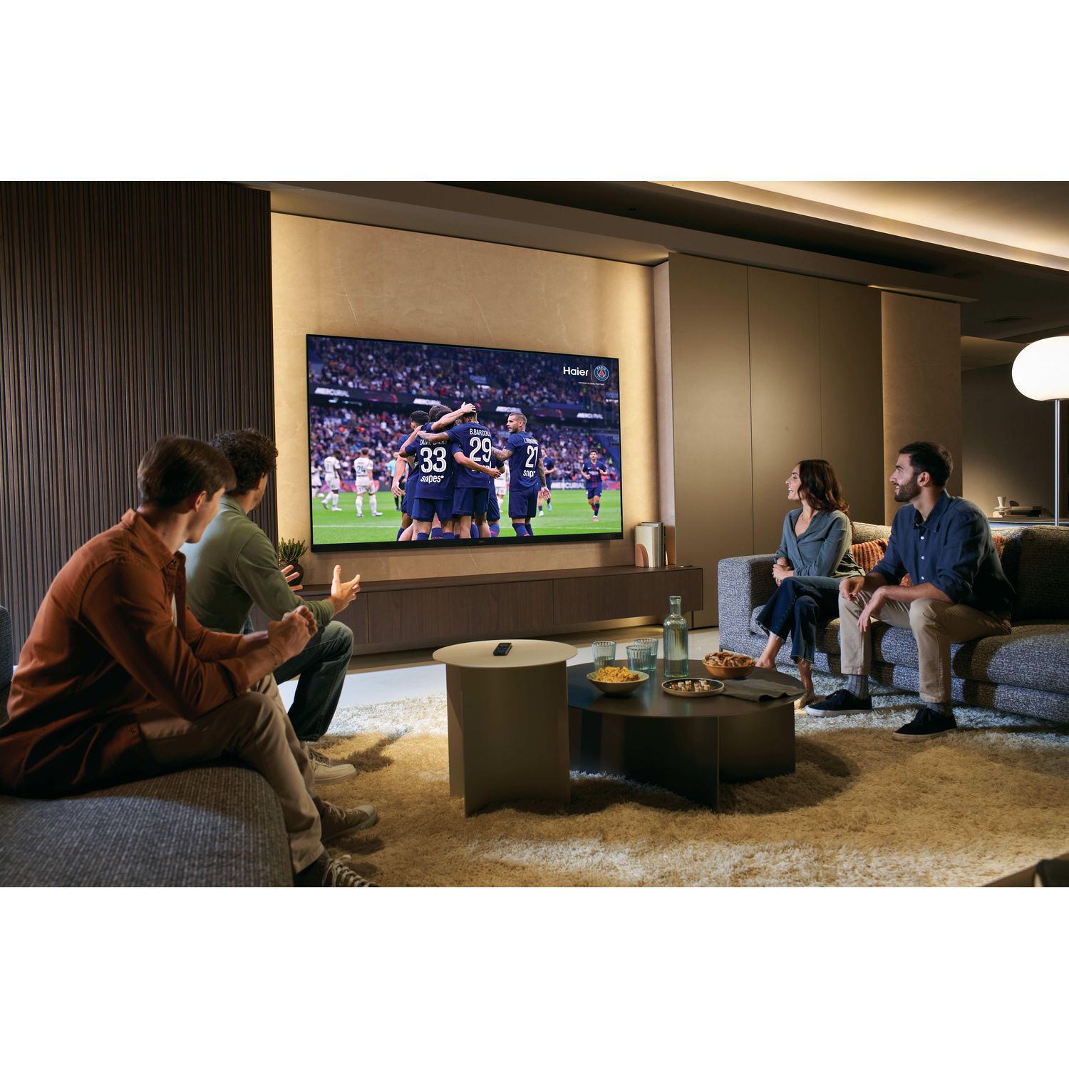 Quattro persone siedono in un soggiorno moderno guardando una partita di calcio in TV.