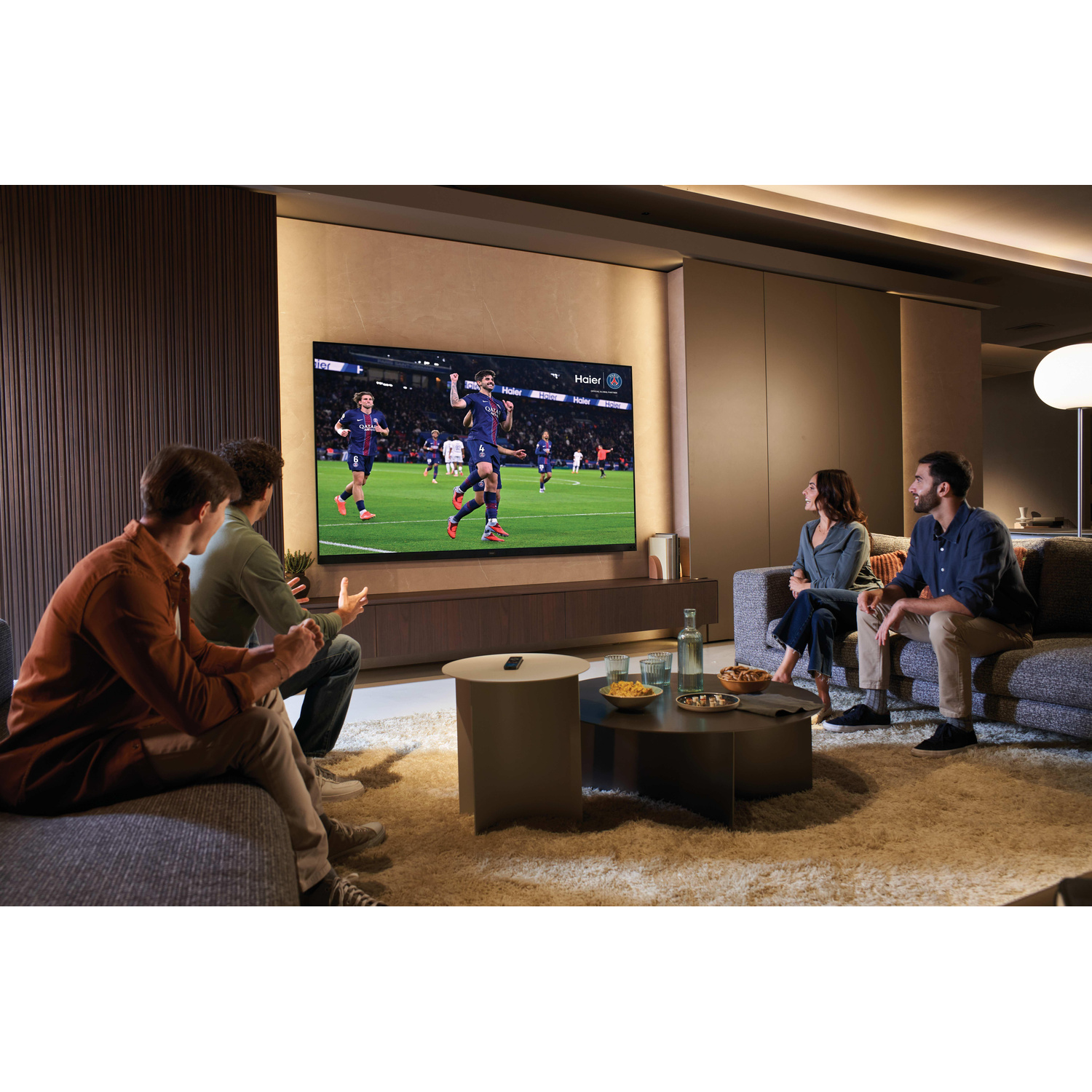 Quattro amici si rilassano sui divani in un soggiorno moderno, guardando una partita di calcio su una grande TV.