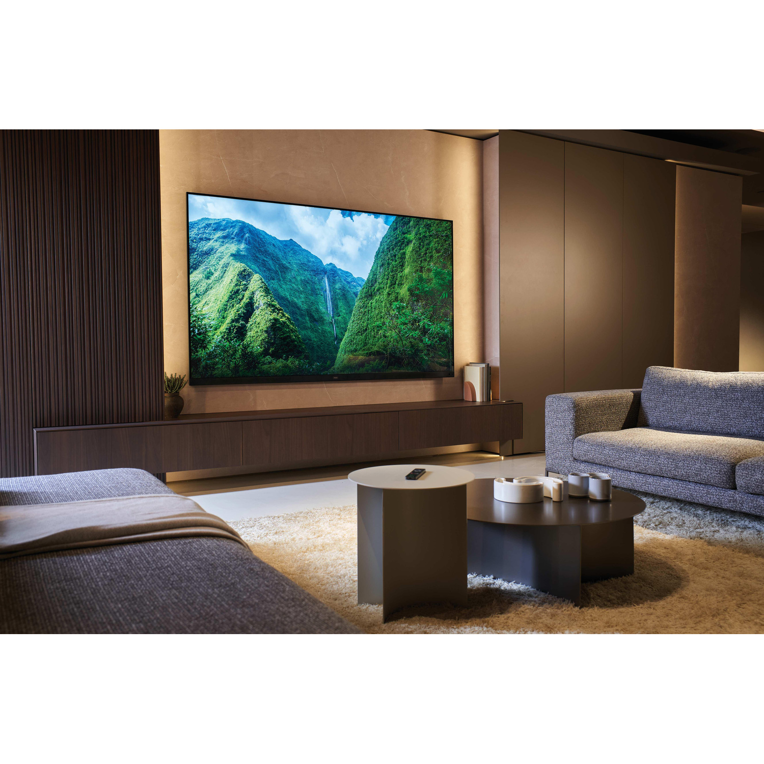 Soggiorno con una grande TV che mostra un paesaggio montano, divani grigi e tavolini da caffè su un tappeto.