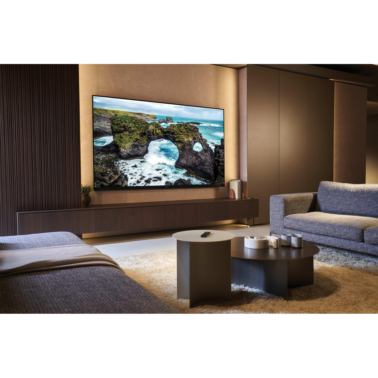 Soggiorno con una grande TV a parete, divani grigi e due tavolini da caffè.