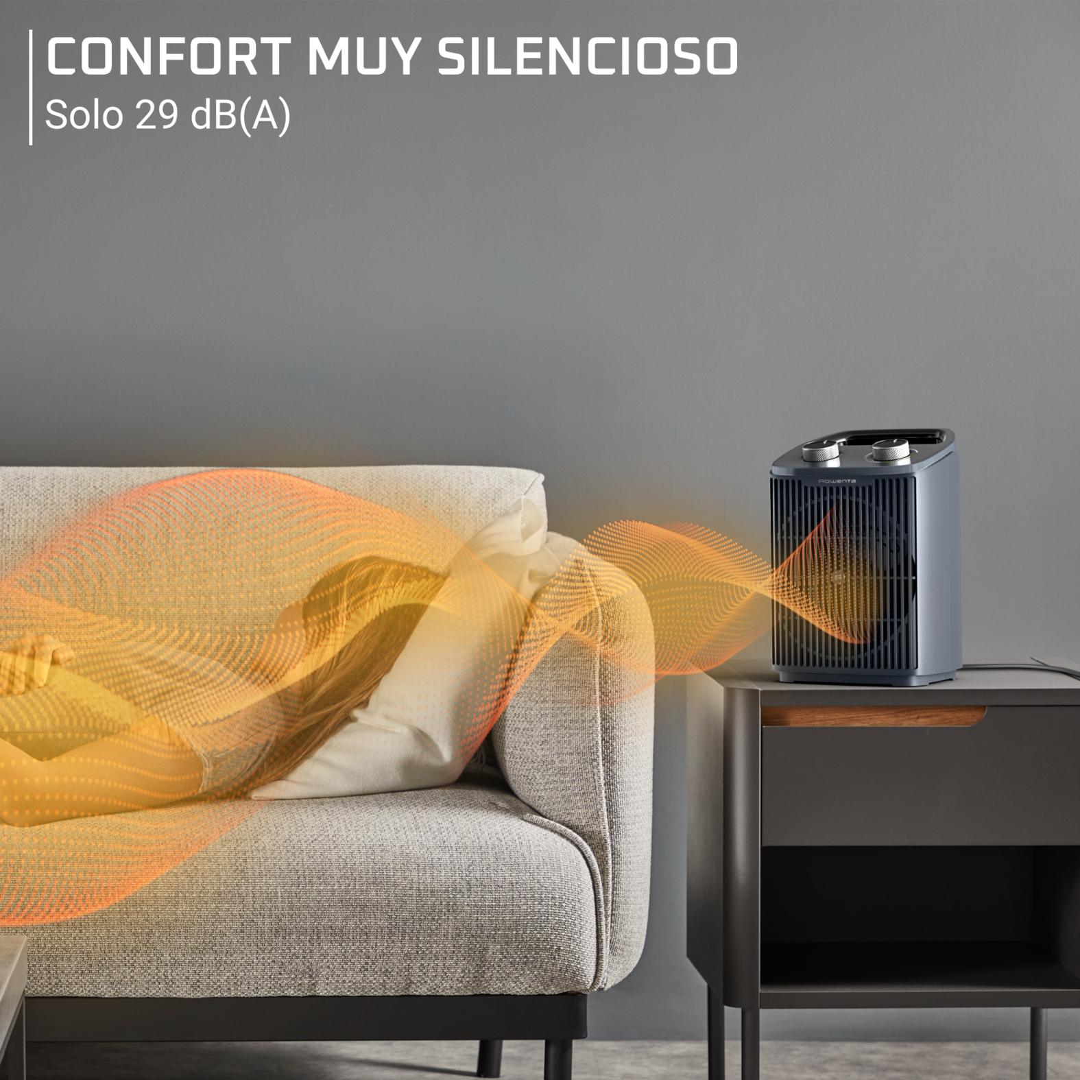 Un calefactor gris en una mesita de noche irradia ondas de calor naranjas hacia una persona durmiendo en un sofá.