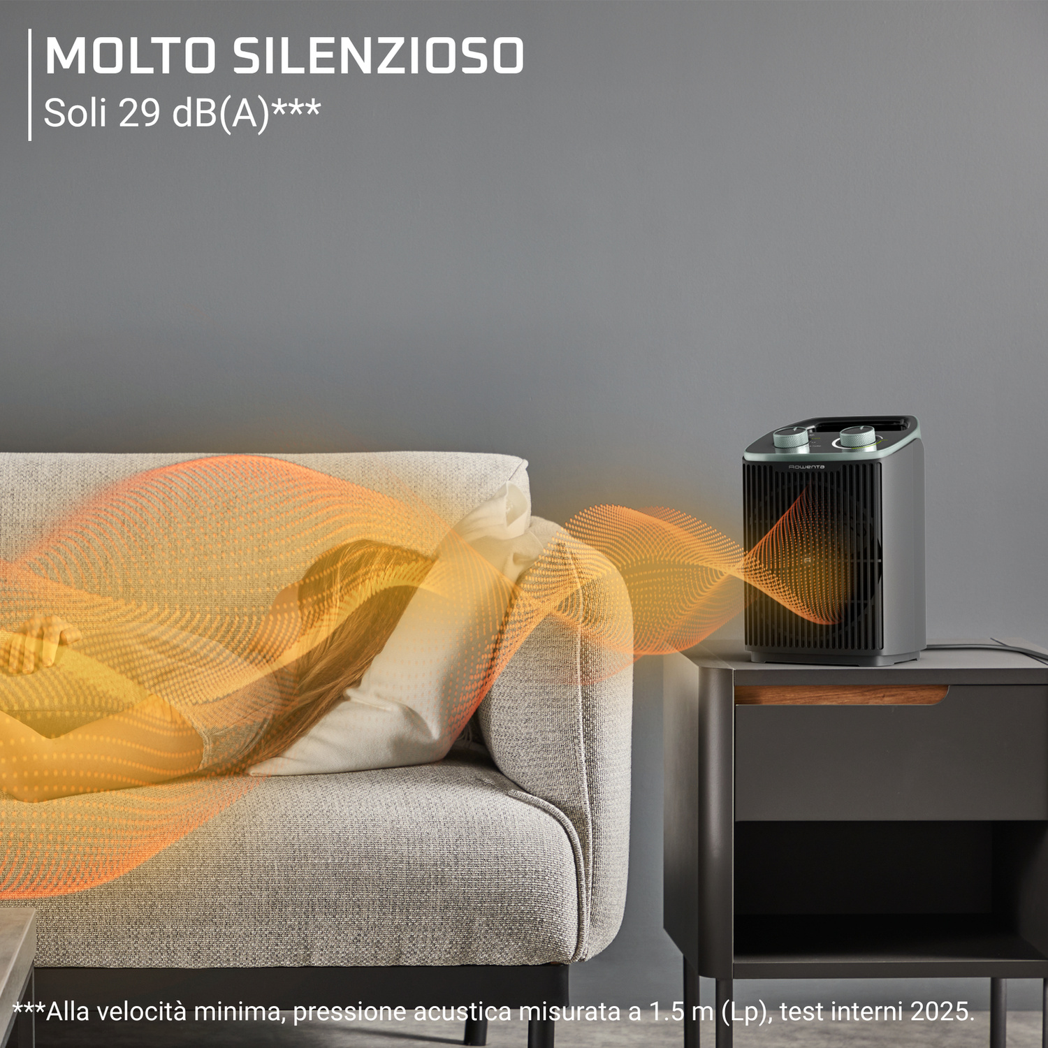 Un termoventilatore portatile su un comodino irradia calore verso una persona che dorme sul divano.