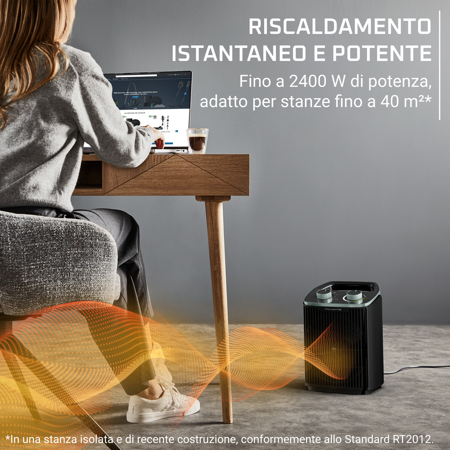 Una donna bionda lavora al pc mentre una stufetta nera emette calore arancione.