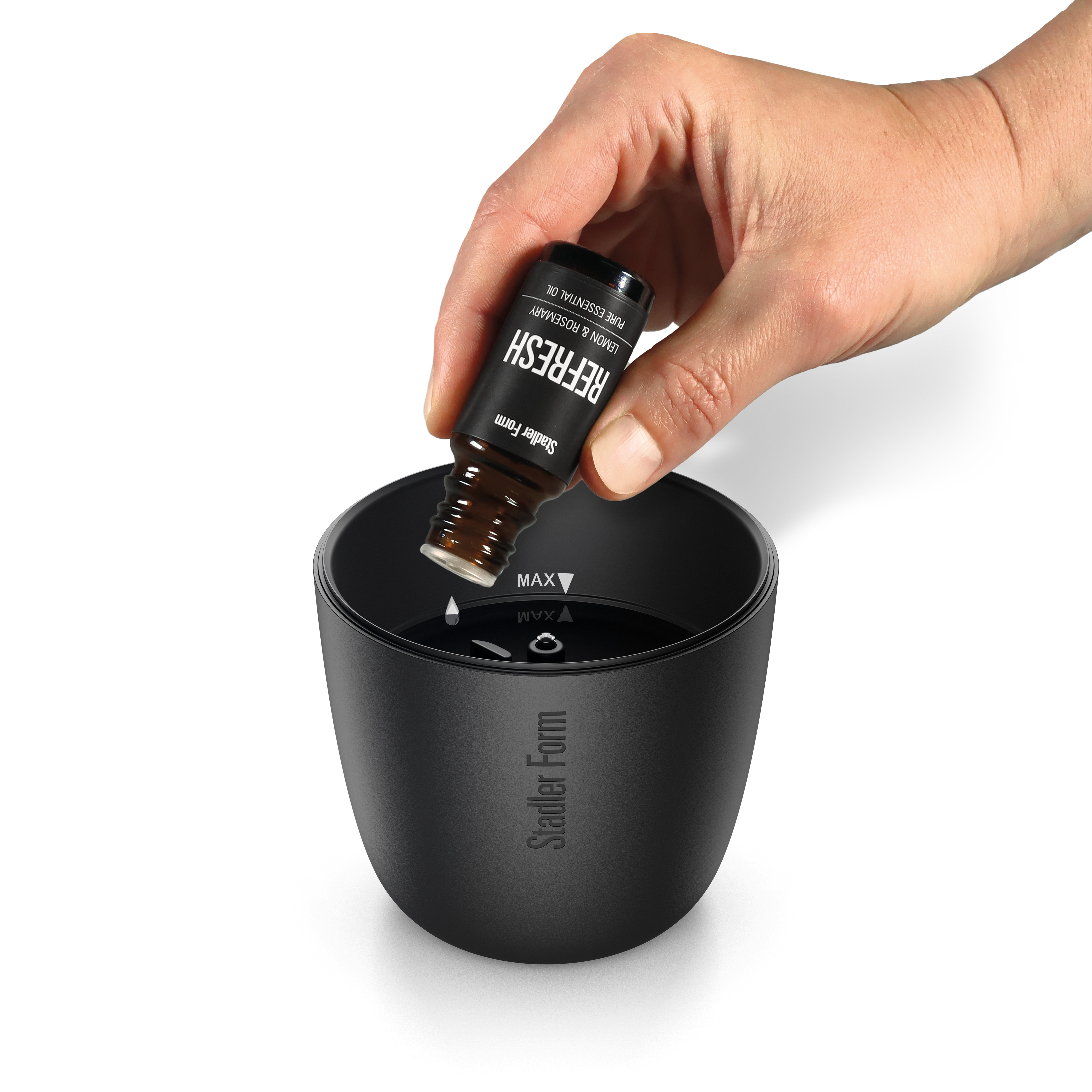 Eine Hand tropft ätherisches Öl in einen schwarzen Stadler Form Diffusor.