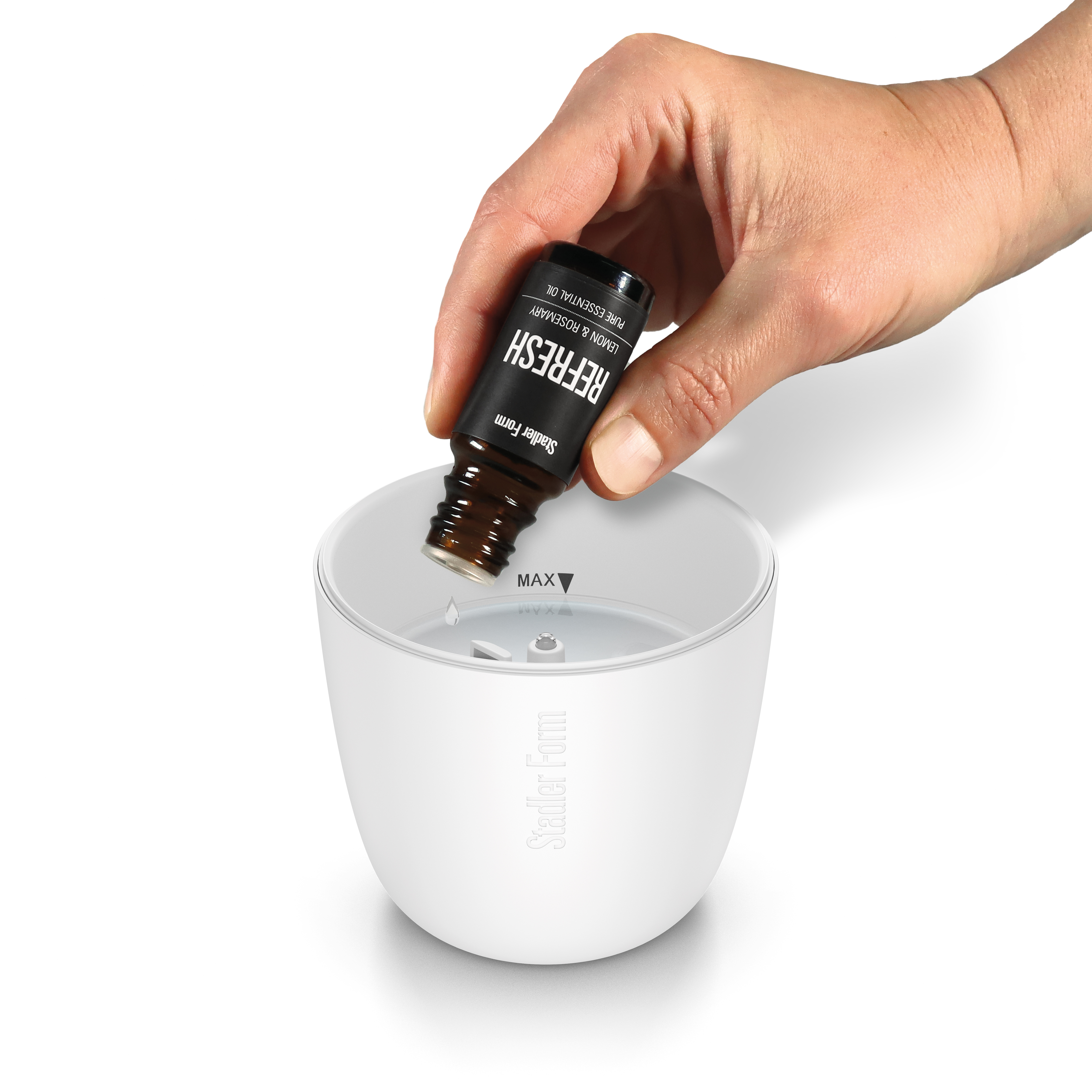 Eine Hand tropft ätherisches Öl aus einer Refresh-Flasche in einen weißen Stadler Form Diffusor.