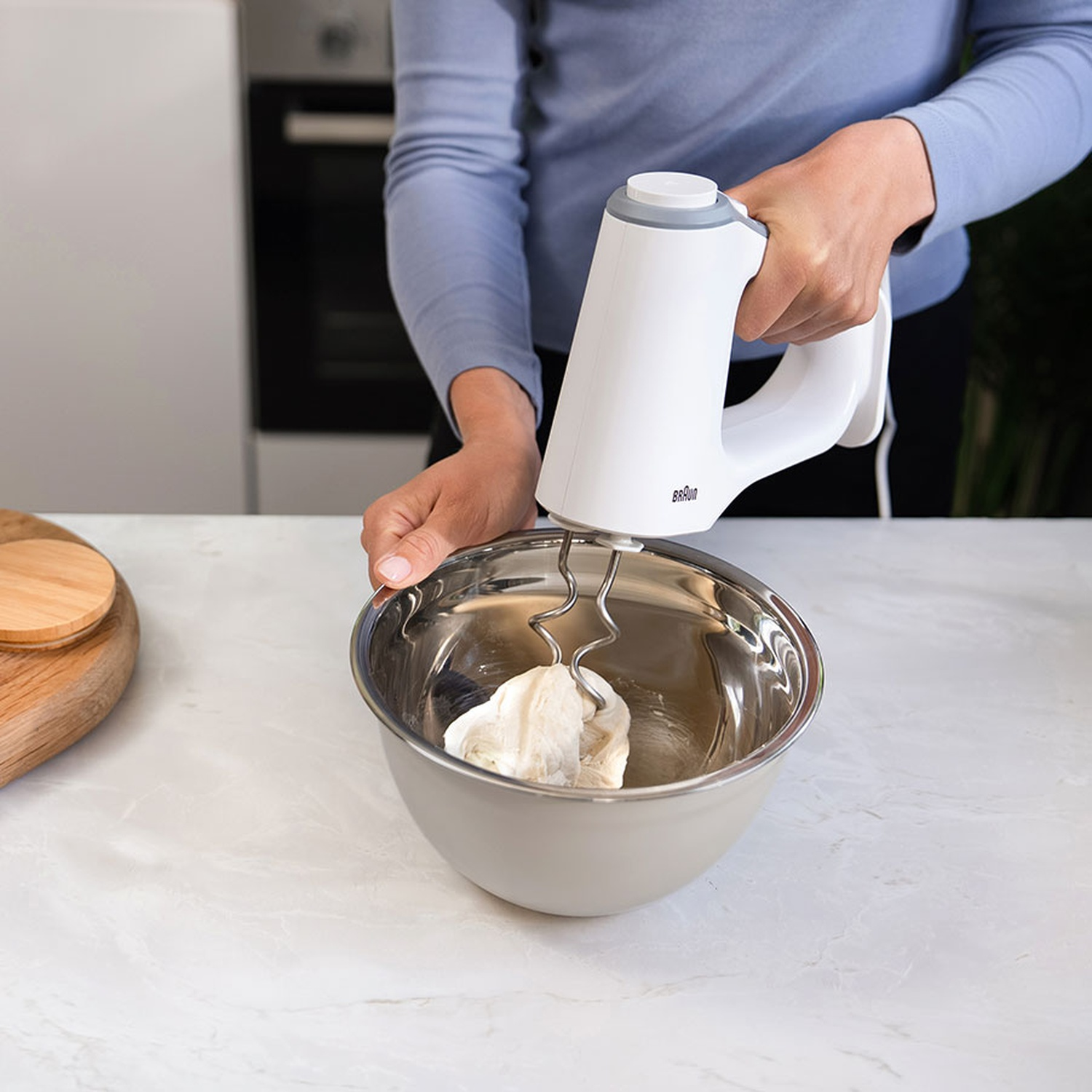 Iemand gebruikt een witte handmixer om deeg te mengen in een roestvrijstalen kom.