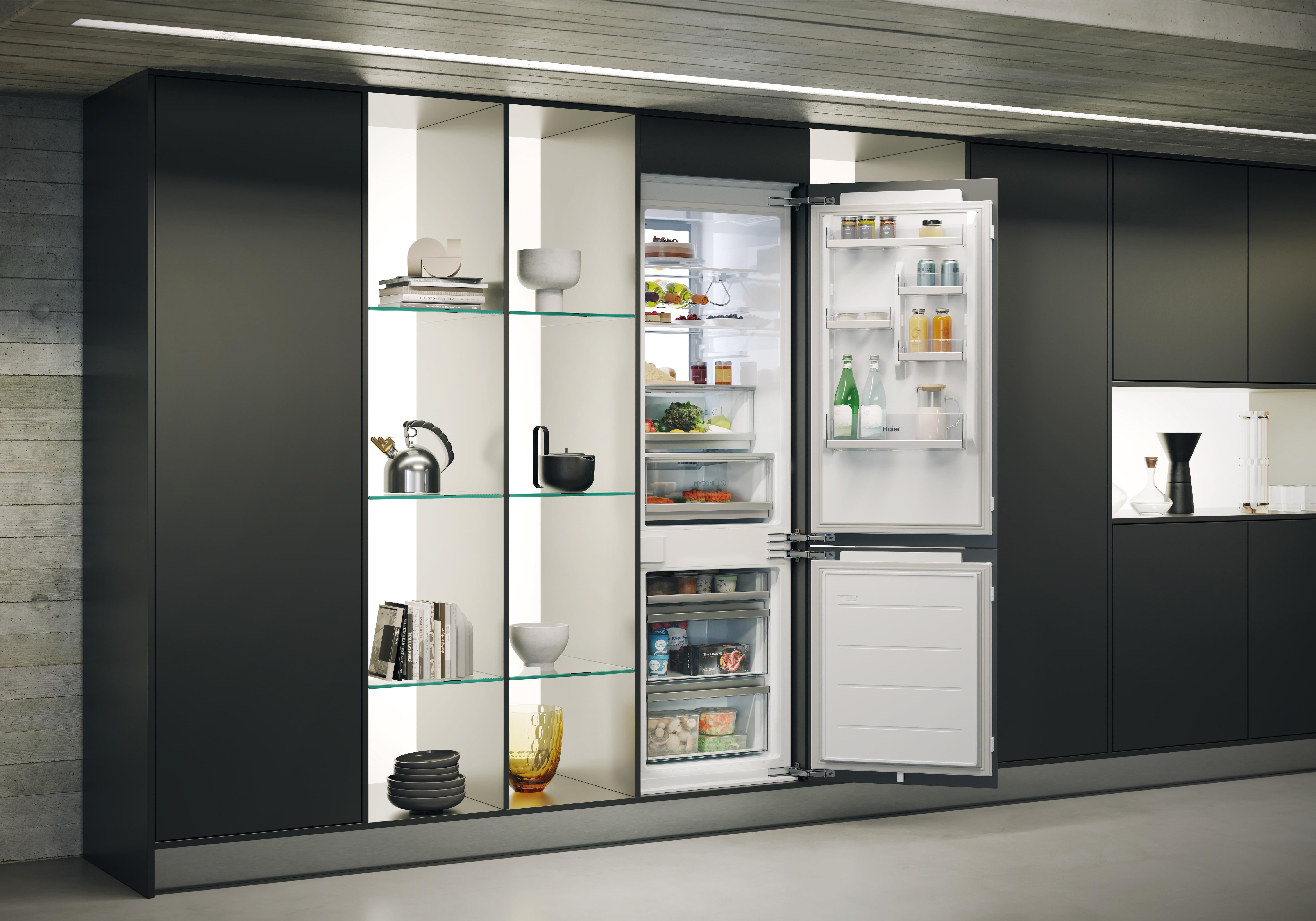 Moderne schwarze Küche mit integriertem, geöffneten Kühlschrank und beleuchteten Regalen voller Dekoration und Geschirr.