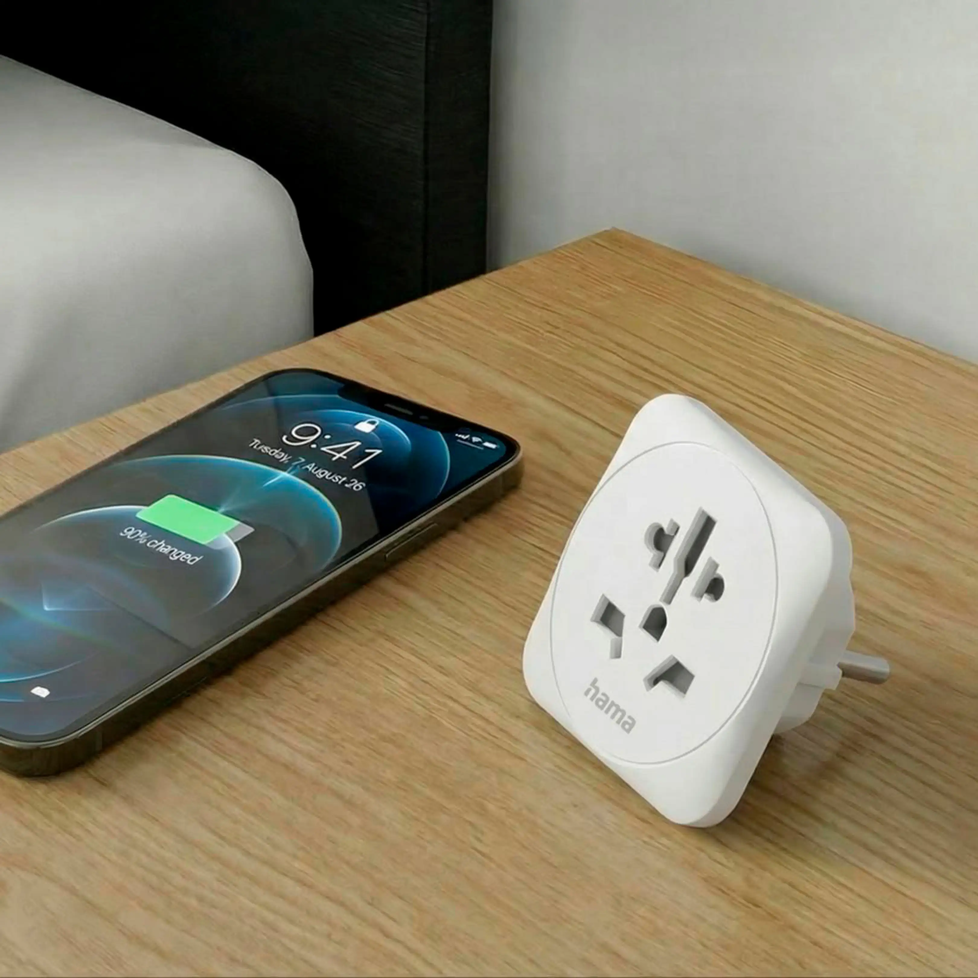 Un adaptador de viaje blanco y un smartphone sobre una mesa de madera.