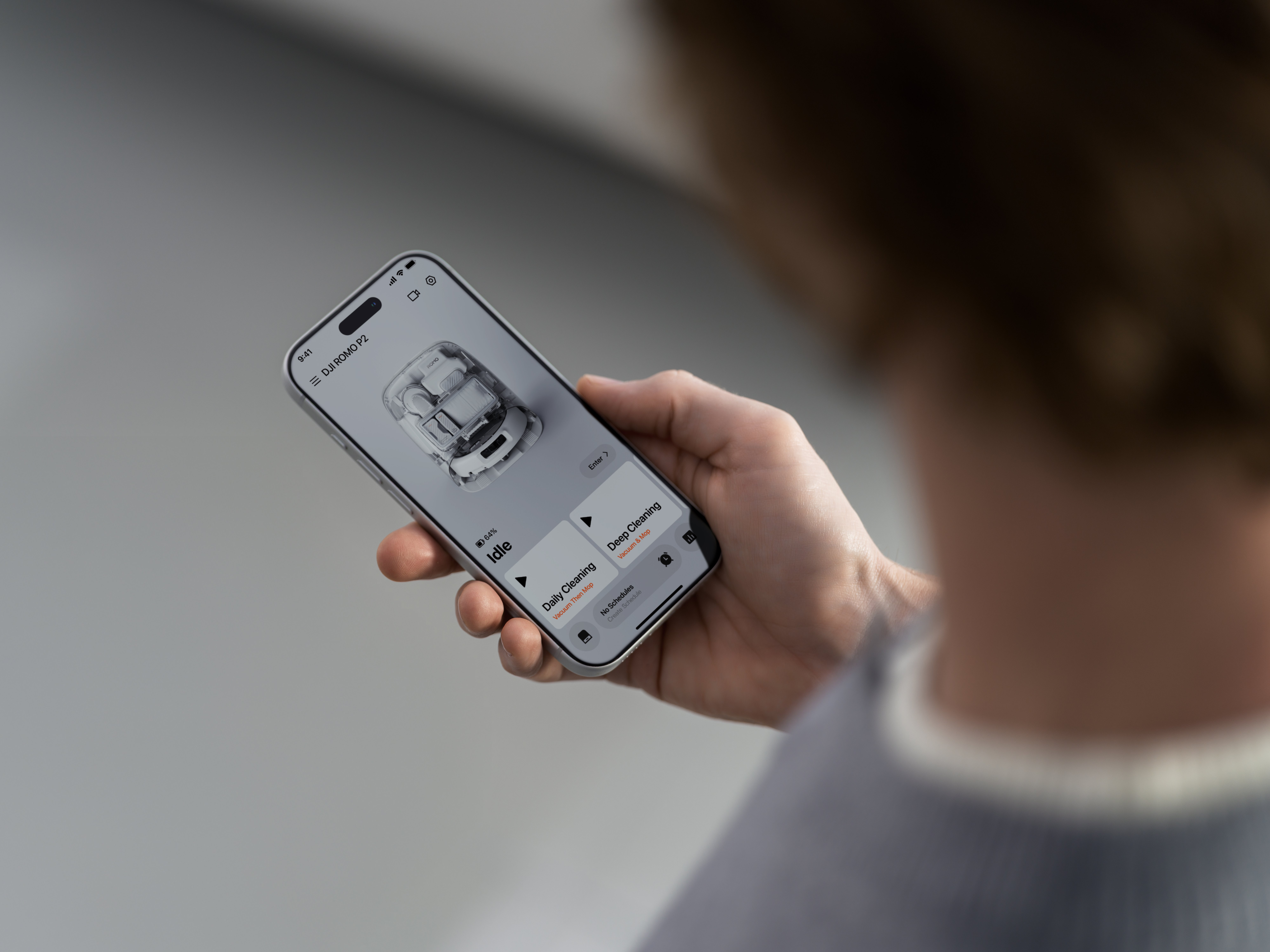 Person hält ein Smartphone, auf dessen Bildschirm die Benutzeroberfläche einer Roboterstaubsauger-App zu sehen ist.