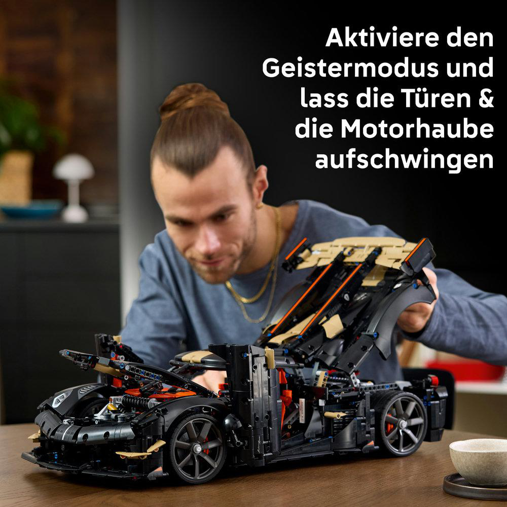 Ein Mann baut ein schwarzes Lego-Technic-Auto mit geöffneten Türen und Haube.