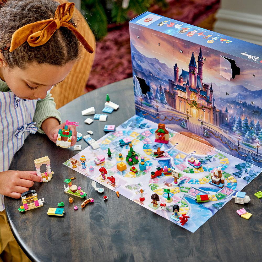 Ein junges Mädchen mit Schleife baut Disney-Lego-Modelle aus einem offenen Adventskalender auf einem Tisch.