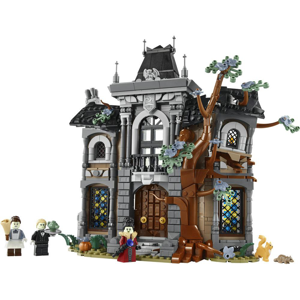 Ein Lego-Spukschloss in Grau und Braun mit bunten Fenstern, einem großen Baum, Minifiguren und Tieren davor.