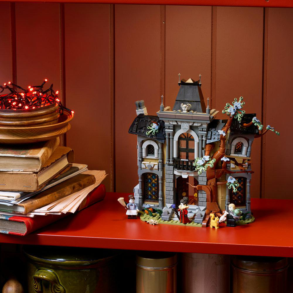 Ein Lego-Spukhausmodell steht auf einem roten Regal neben alten Büchern und einer Schale mit roten Lichtern.