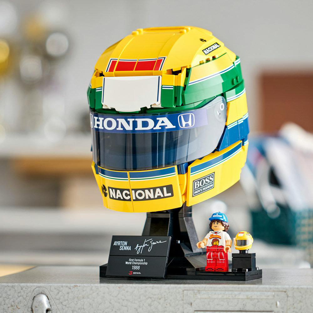 Ein Lego-Modell von Ayrton Sennas gelb-grün-blauem Helm mit einem Ständer, einer Namensplakette und einer kleinen Figur.