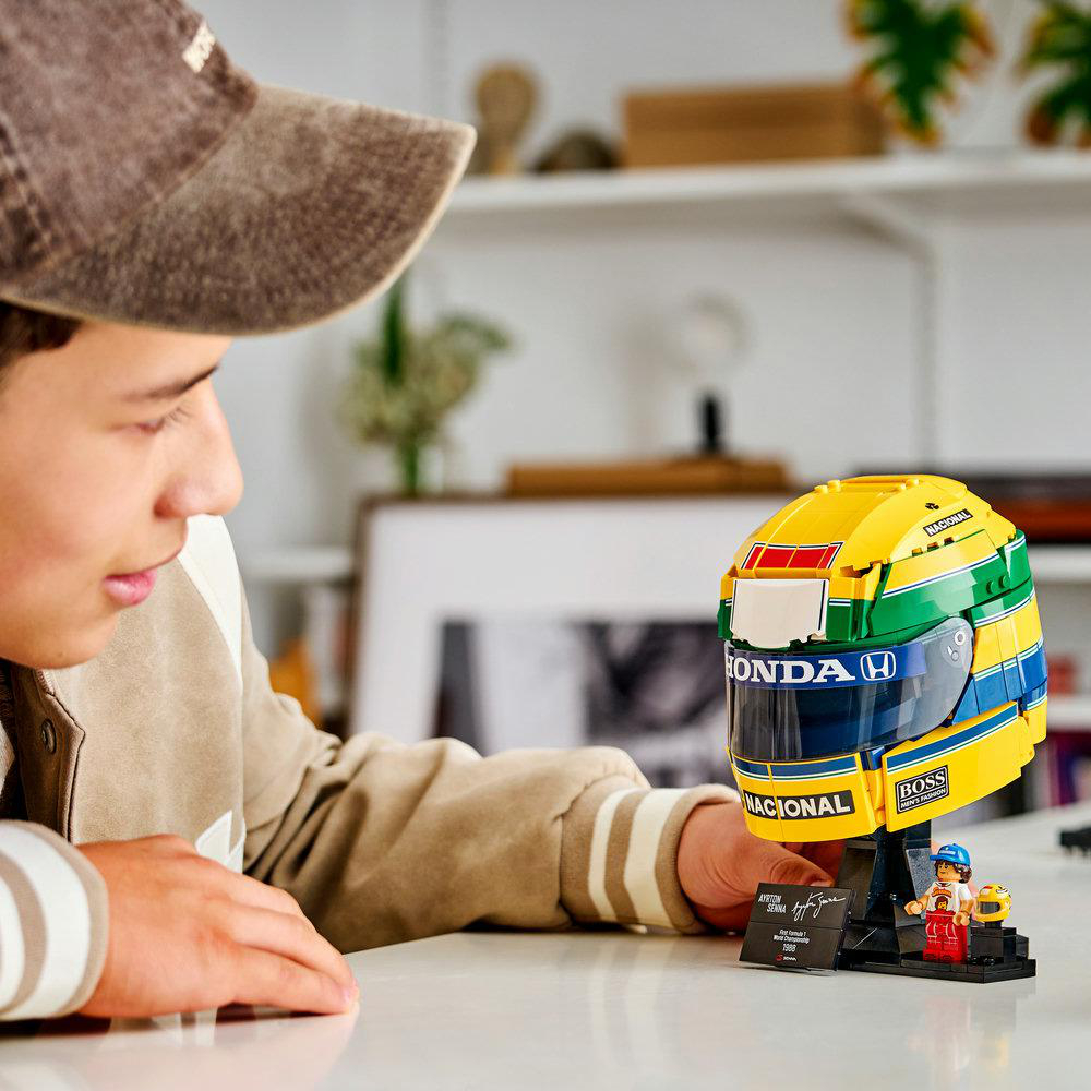 Ein Junge betrachtet einen detaillierten Lego-Rennhelm von Ayrton Senna auf einem weißen Tisch.