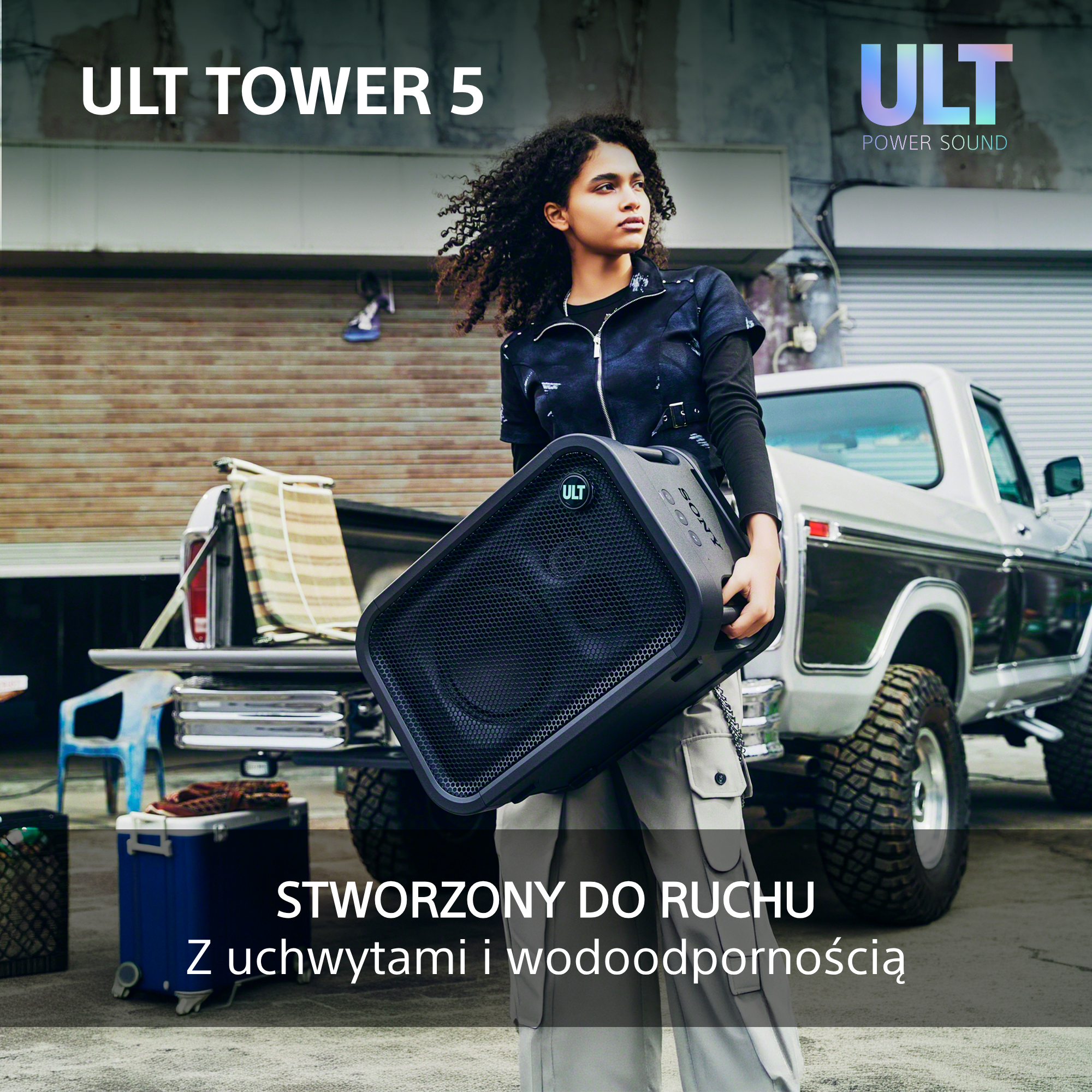 Kobieta niesie czarny głośnik ULT TOWER 5 na zewnątrz przed białym pick-upem.