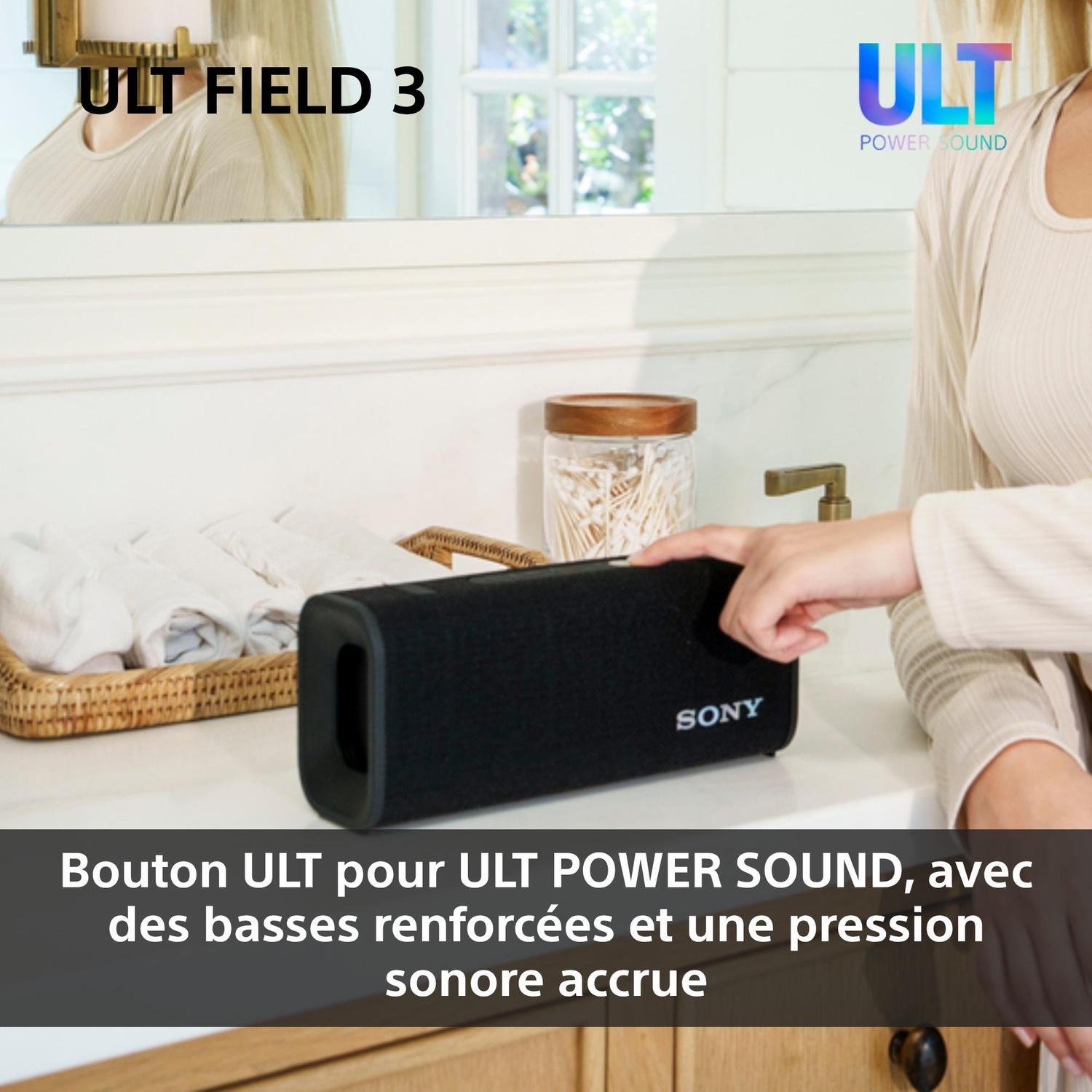 Une femme appuie sur une enceinte Bluetooth Sony noire sur un comptoir de salle de bain blanc avec des serviettes.