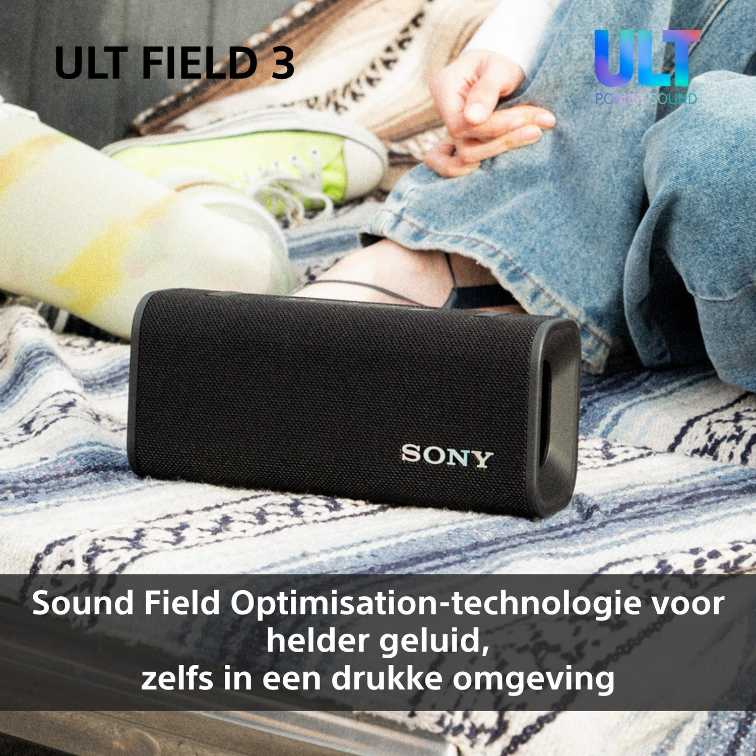 A black Sony bluetooth speaker rests on a blue and white striped blanket next to seated people.