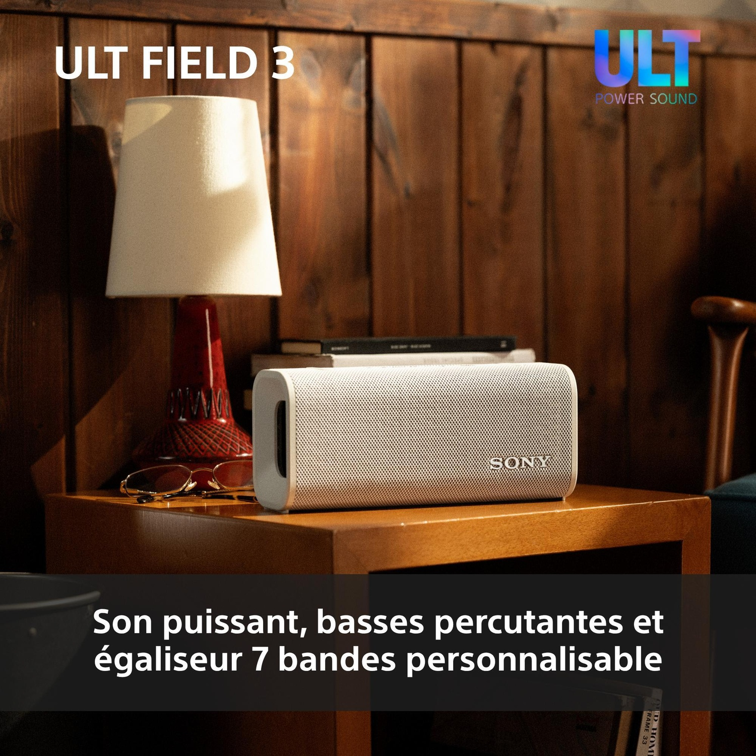 Une enceinte Bluetooth Sony blanche sur une table de chevet en bois avec une lampe et des livres.