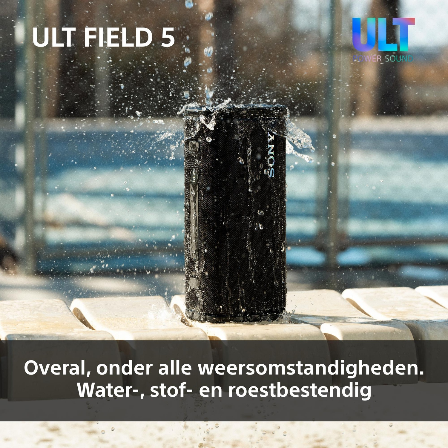 A black Sony ULT FIELD 5 Bluetooth speaker is being splashed with water while standing on a light-colored bench.