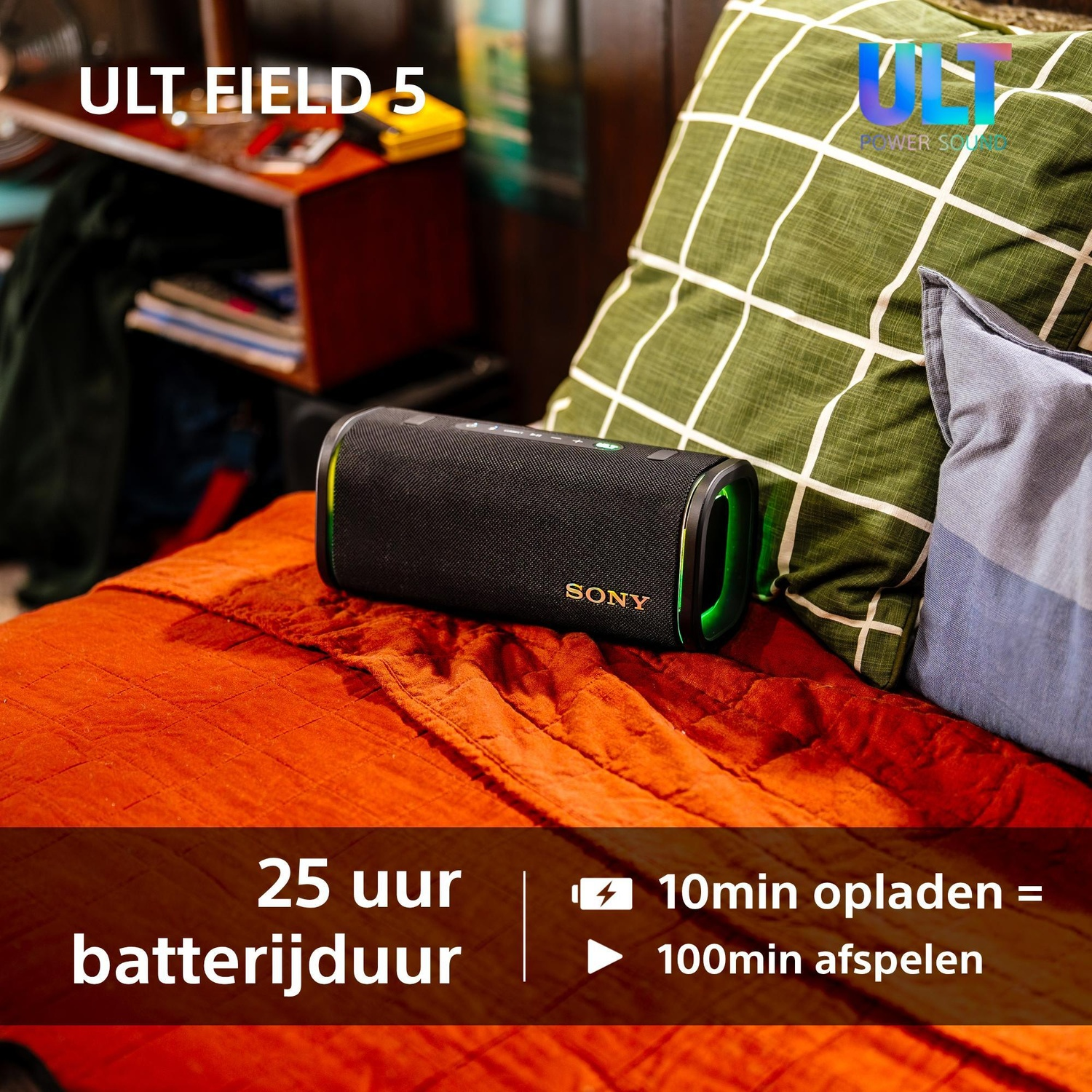 A black Sony bluetooth speaker rests on an orange bed beside green and blue pillows.
