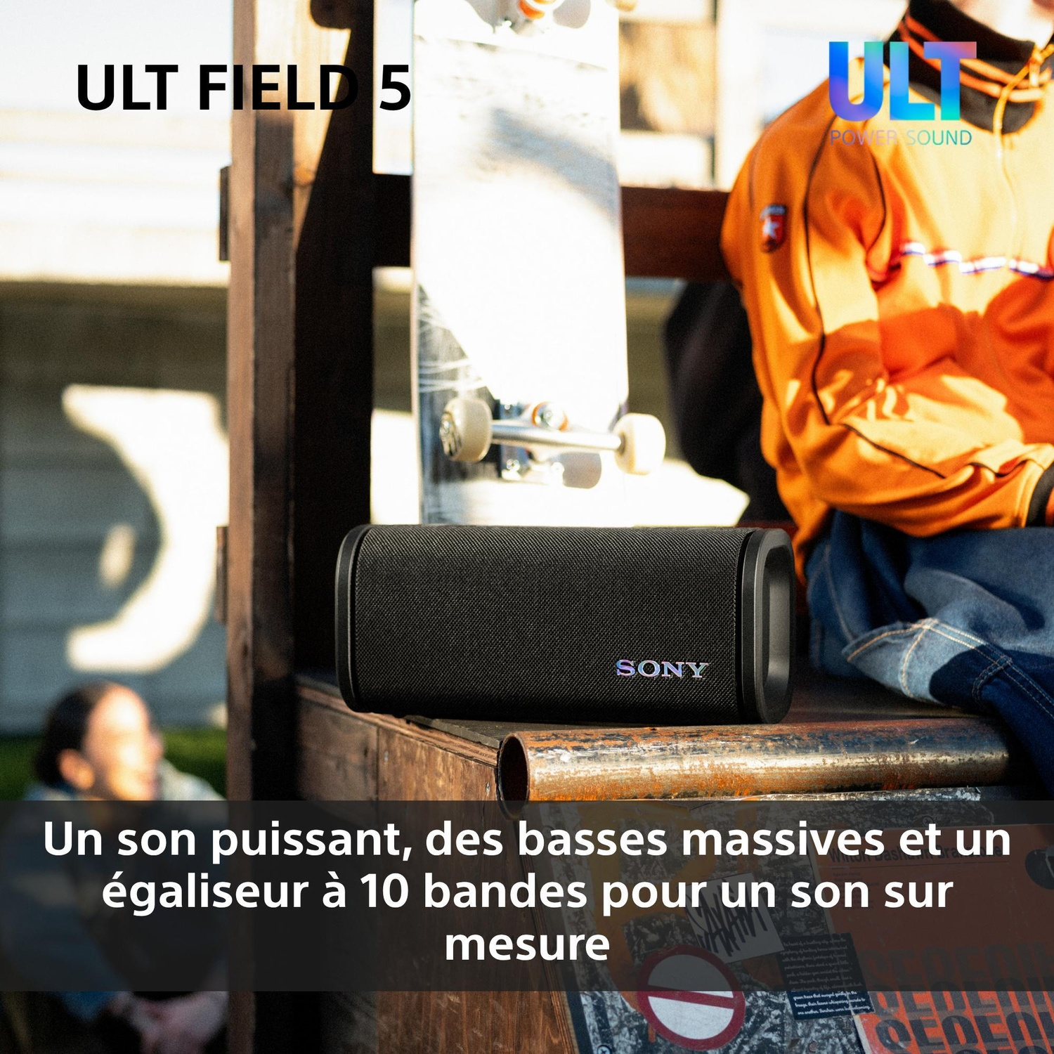 Une enceinte portable Sony noire repose sur une rampe en bois à l'extérieur près d'un skateboard et d'une personne.