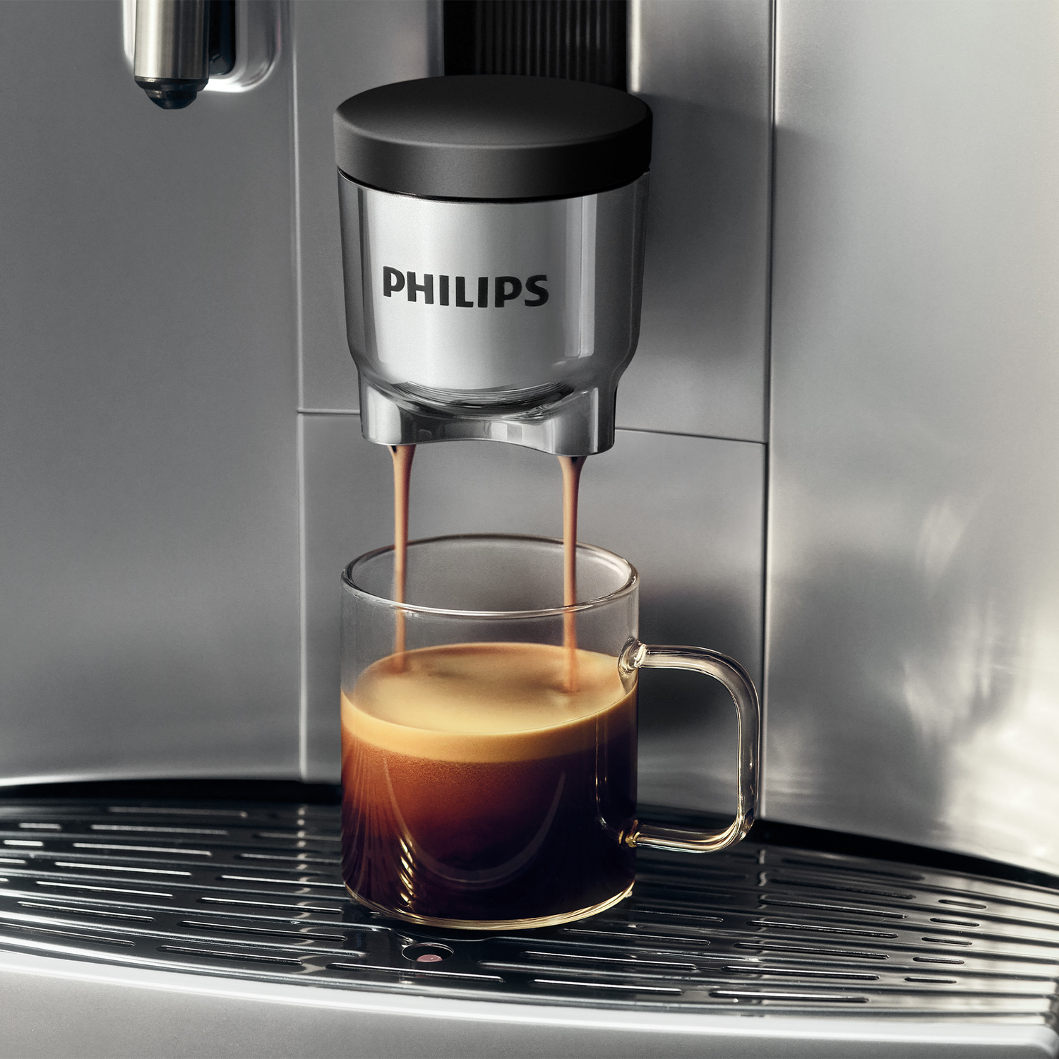 A Philips coffee machine pours fresh espresso into a clear glass mug on a silver drip tray.