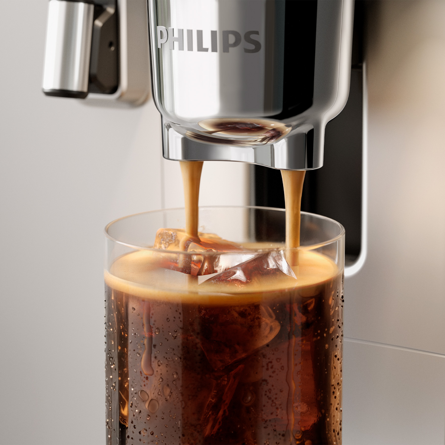 A Philips coffee machine dispenses espresso into a glass filled with ice cubes against a light background.