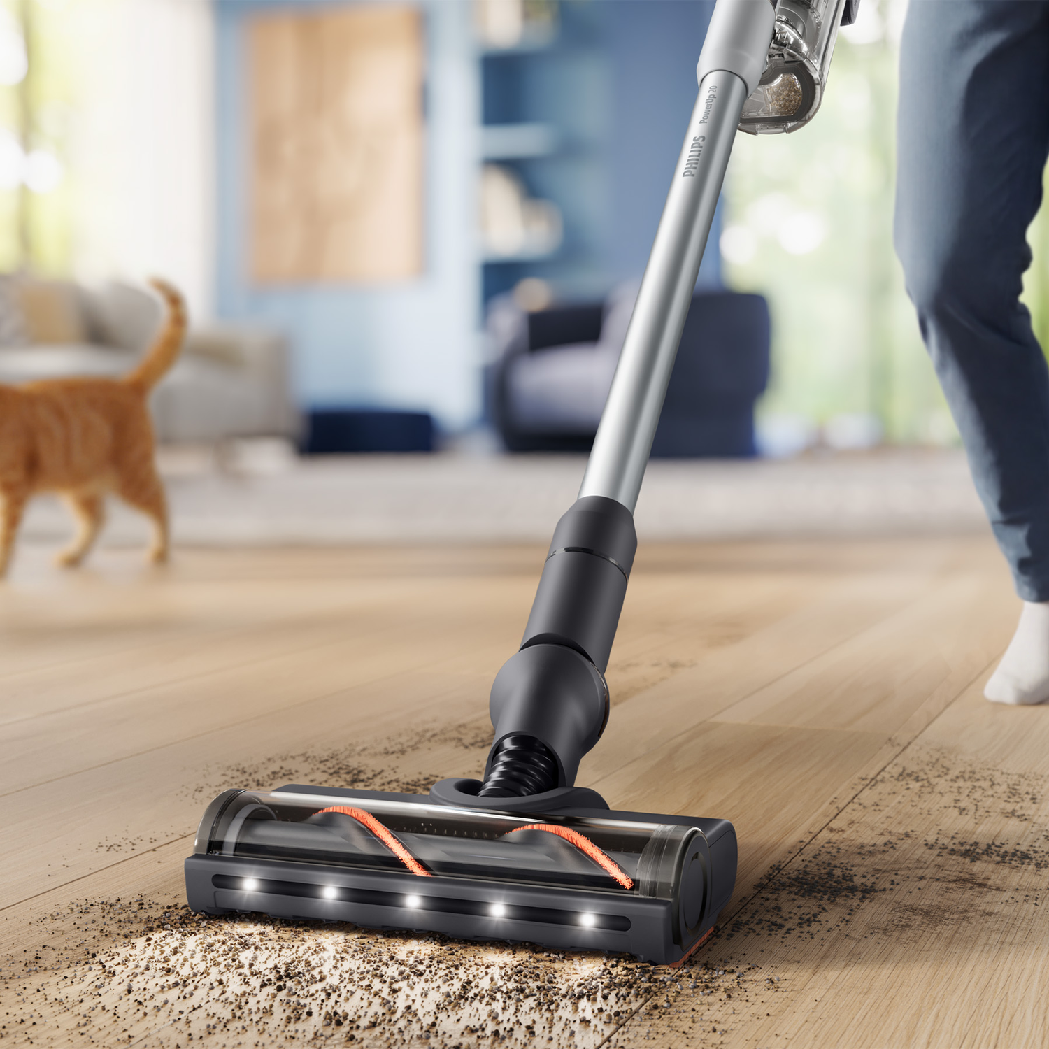 A vacuum cleaner cleans dirt from a wooden floor in a room, with a cat visible in the blurred background.