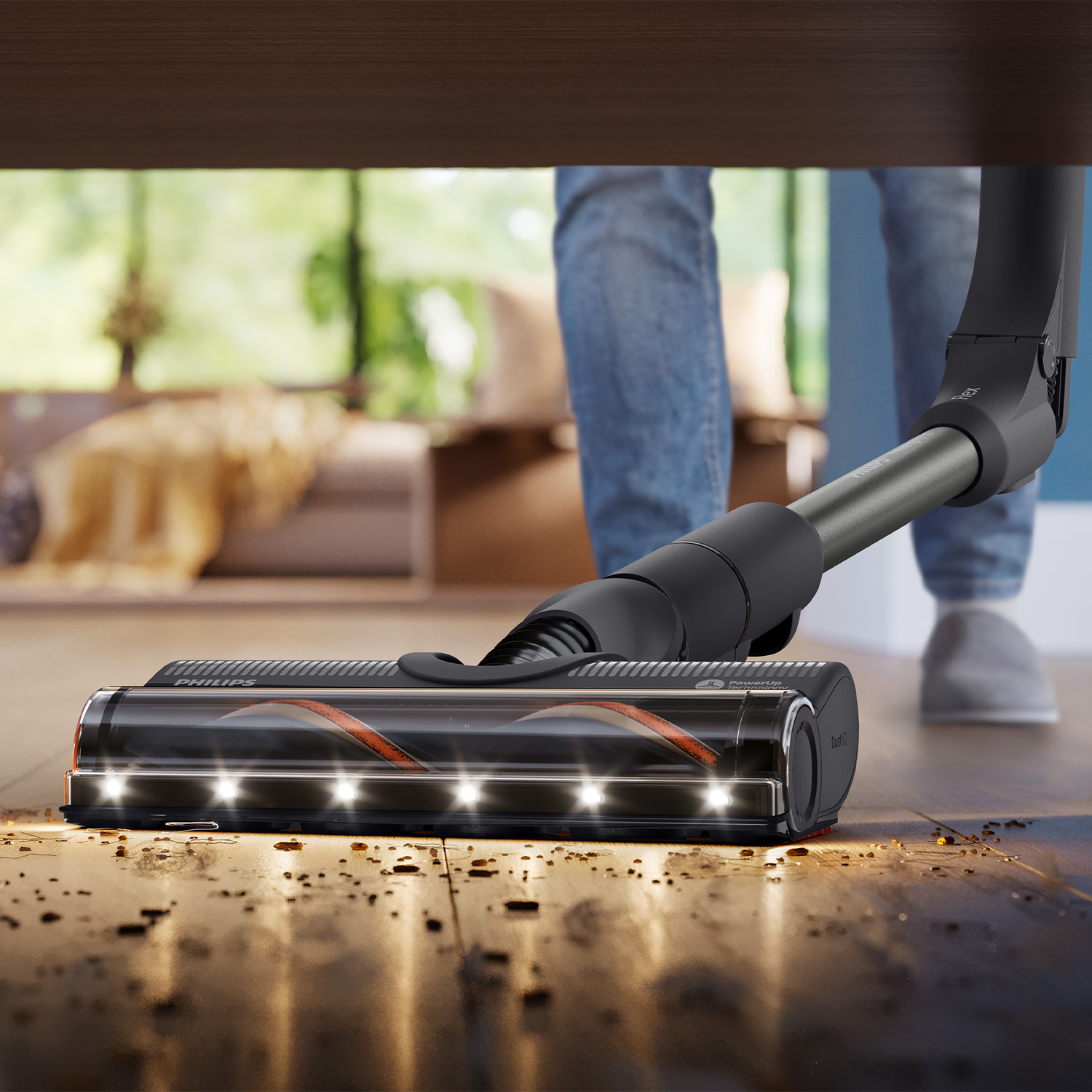 A Philips vacuum cleaner with LEDs cleans dirt on the wooden floor under a table.