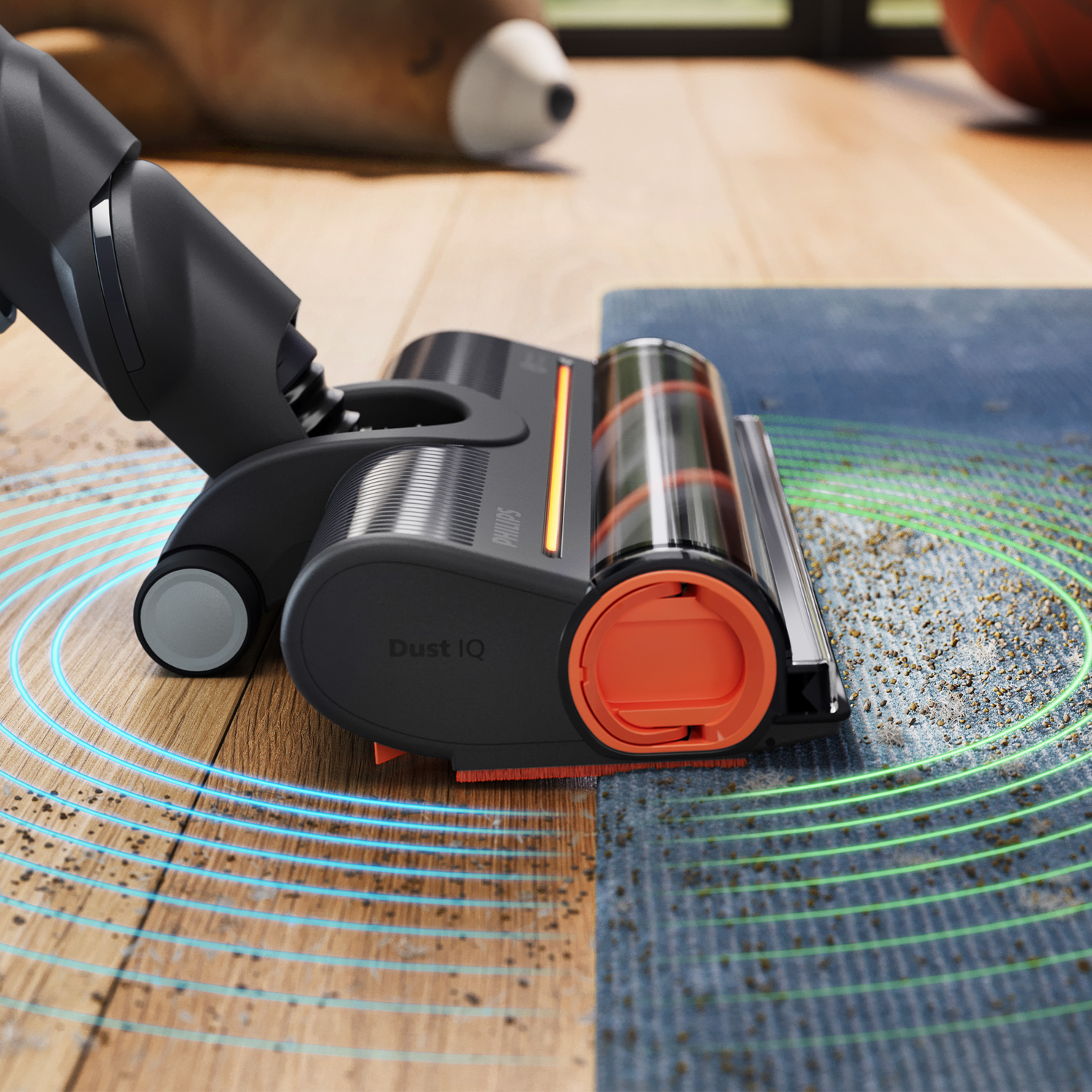 A dark gray and orange vacuum cleaner head cleans a blue rug and wooden floor with glowing detection waves.