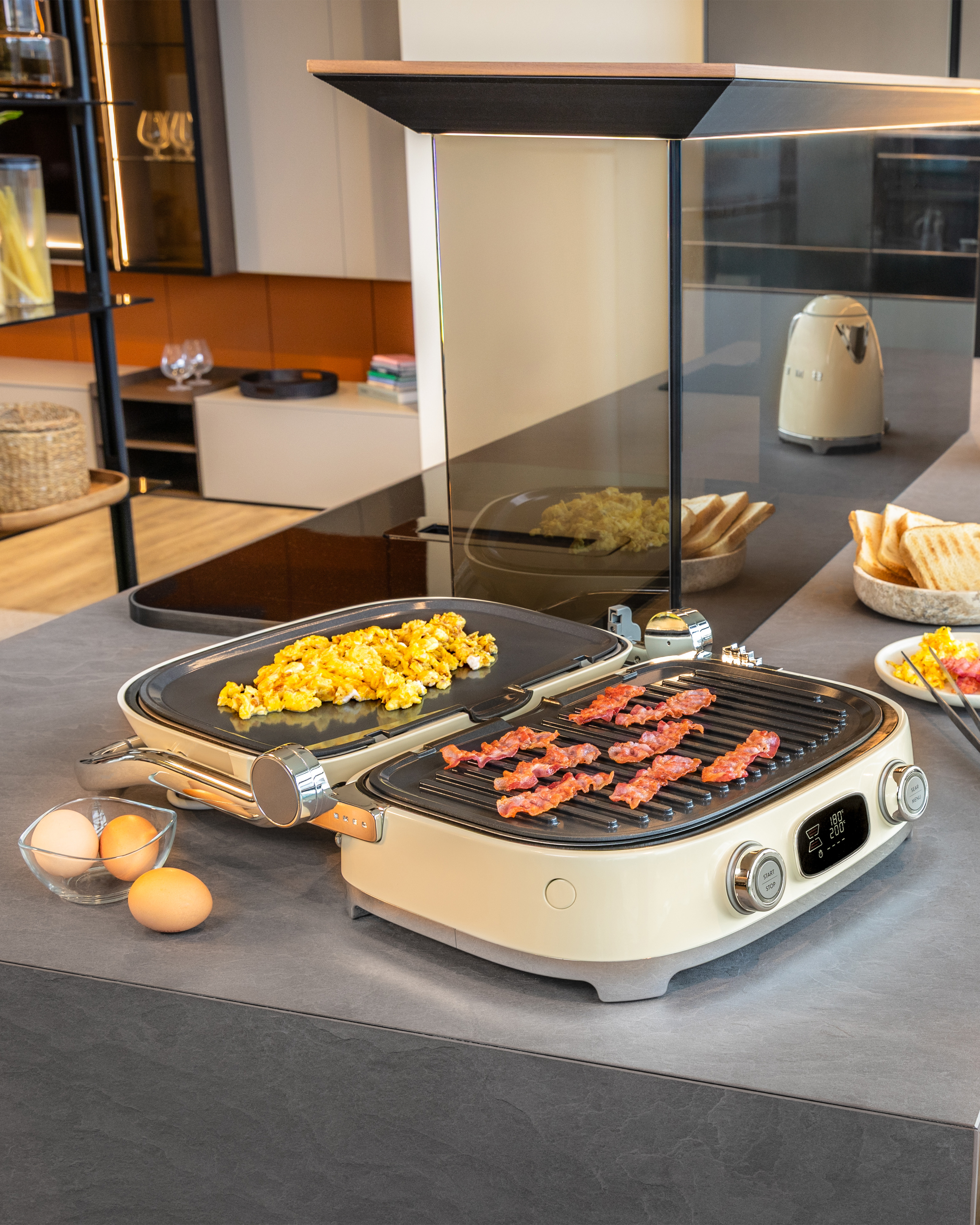 Ein offener elektrischer Grill mit Rührei und Speck auf einer modernen Küchentheke.