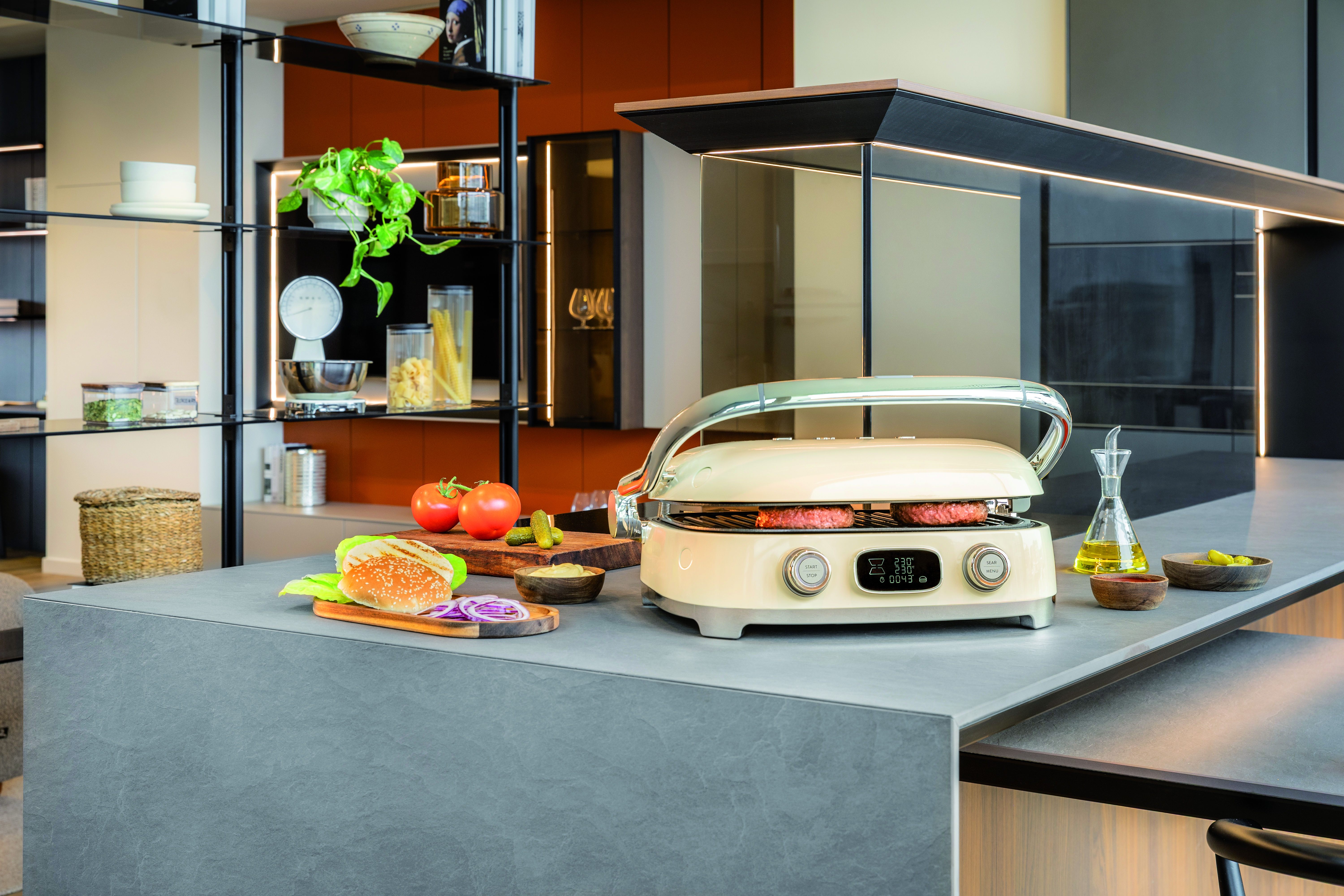 Ein beiger Elektrogrill auf einer Küchentheke mit Burgut-Zutaten und Regalen im Hintergrund.