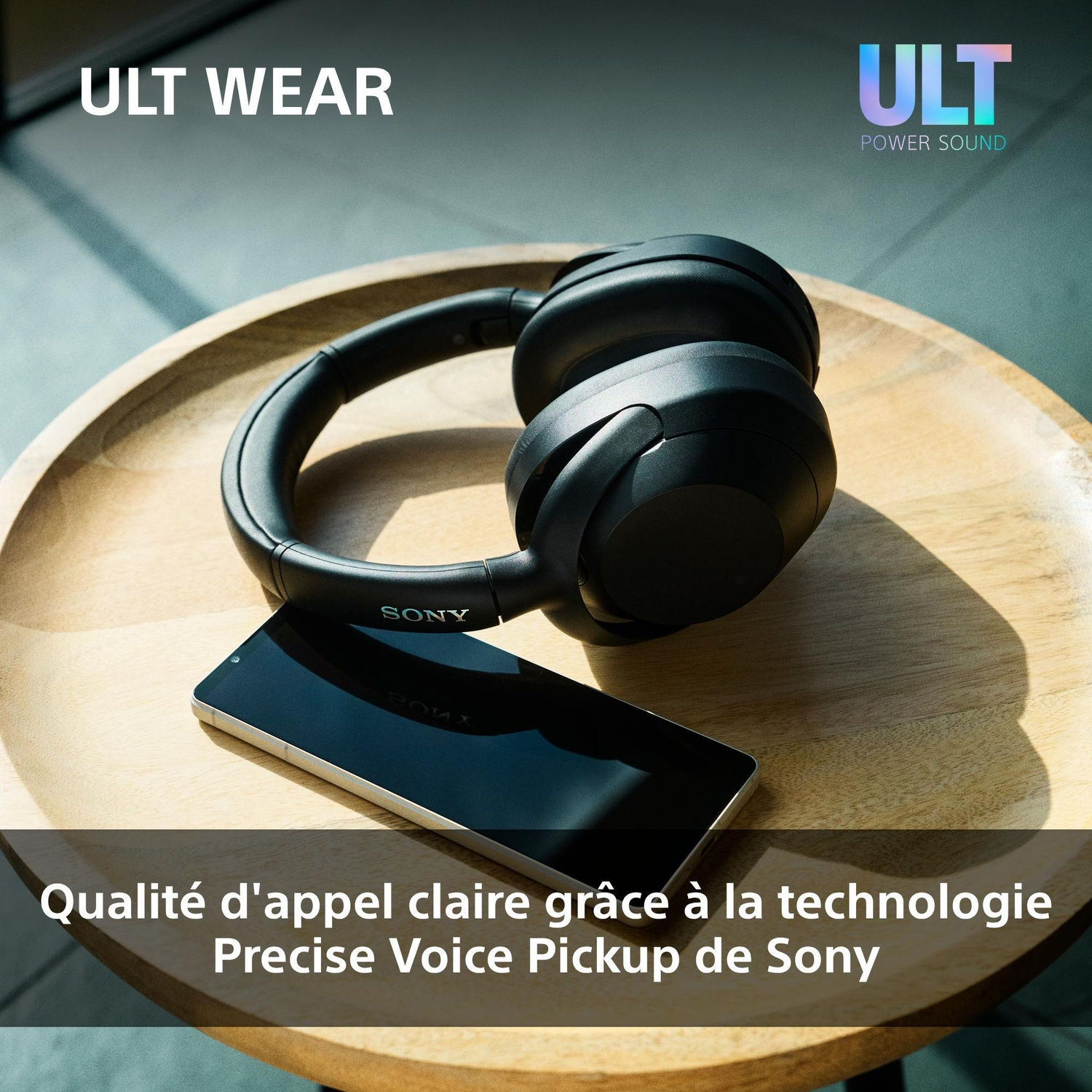 Des écouteurs sans fil Sony noirs reposent sur un plateau en bois à côté d'un smartphone.
