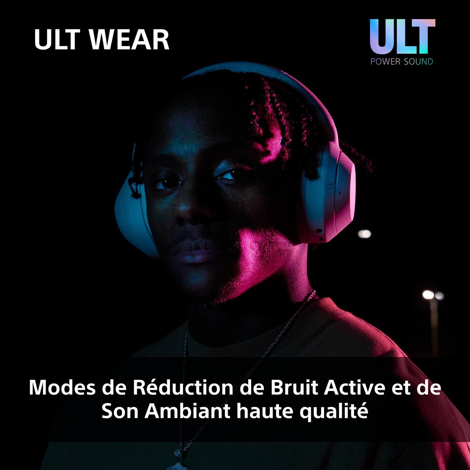 Un homme portant des écouteurs blancs se tient dans le noir, illuminé par une lumière néon.