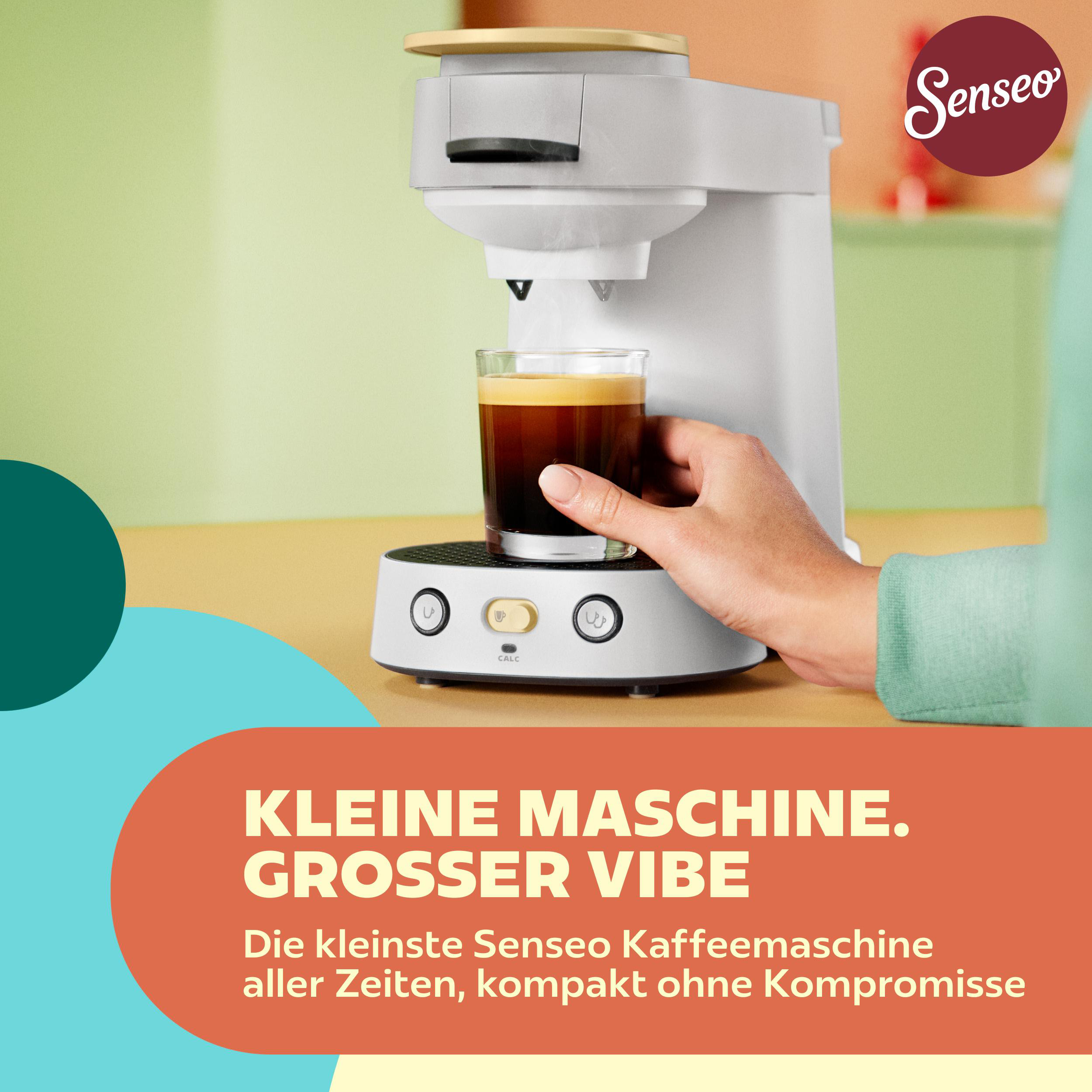 Eine Hand greift nach einem Glas frisch gebrühtem Kaffee unter einer kompakten weißen Senseo-Kaffeemaschine.