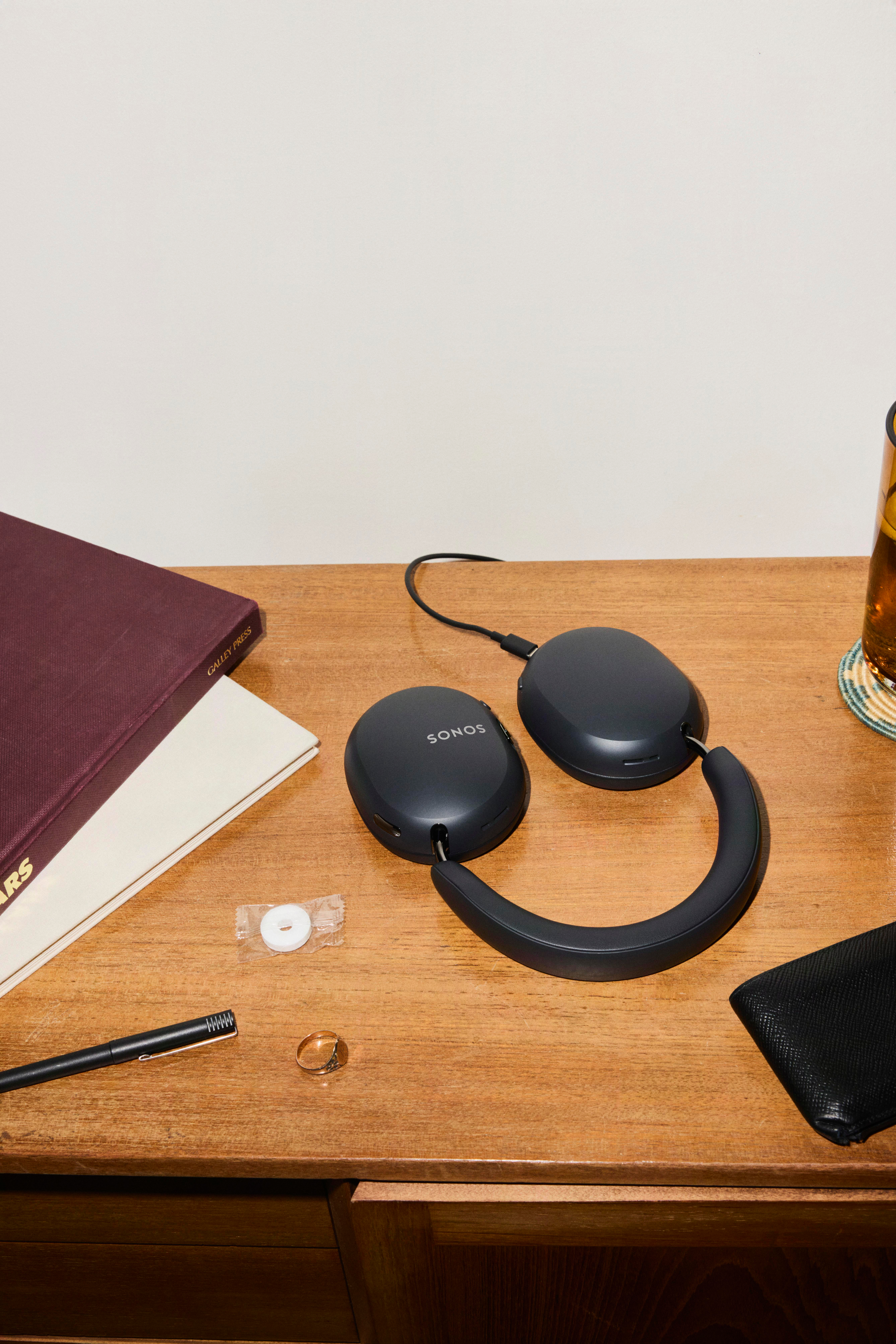 Schwarze Sonos-Kopfhörer, Stifte, Bücher und ein Ring liegen auf einem Holztisch.