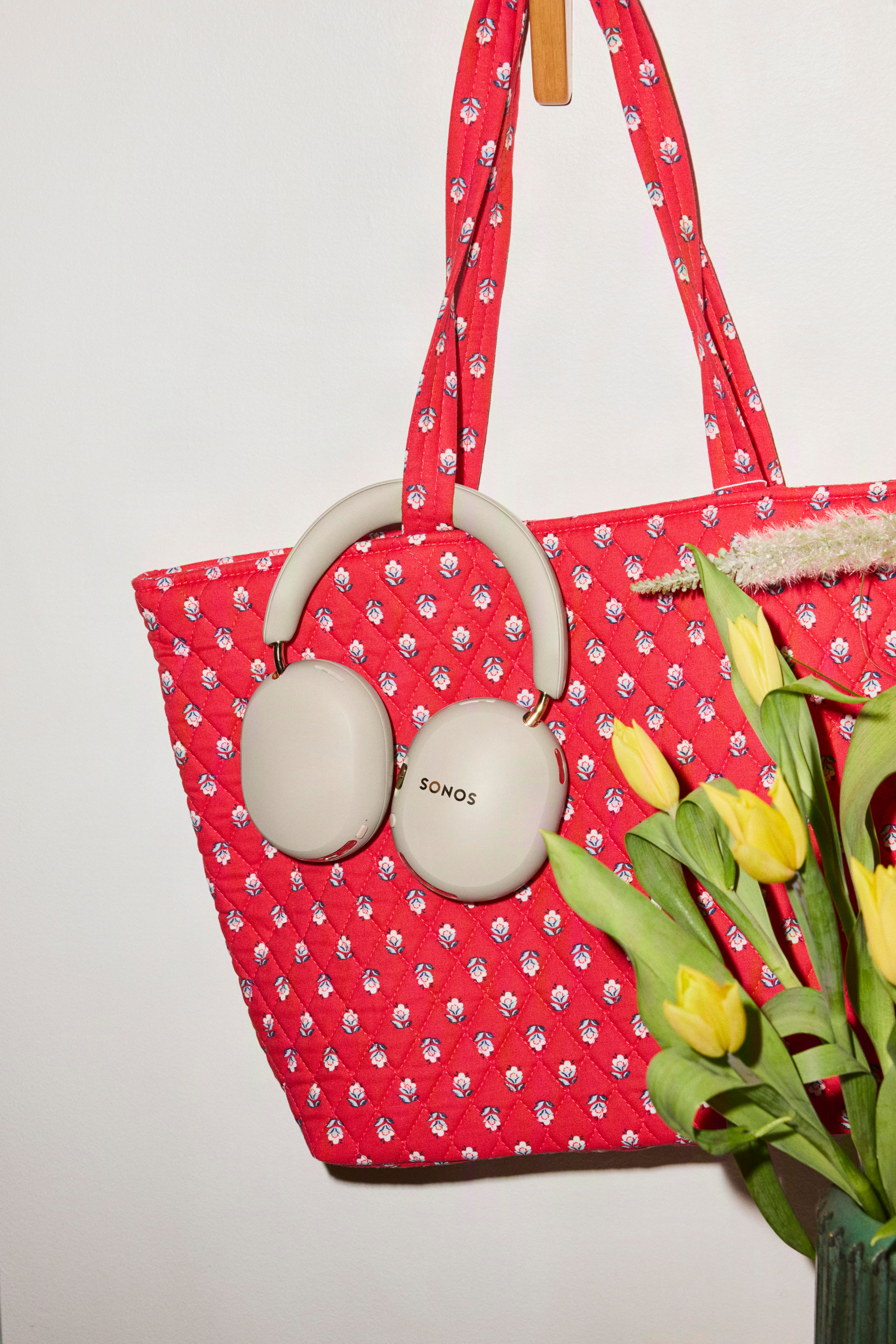 Beige Kopfhörer hängen an einer roten Blumentasche, daneben gelbe Tulpen.