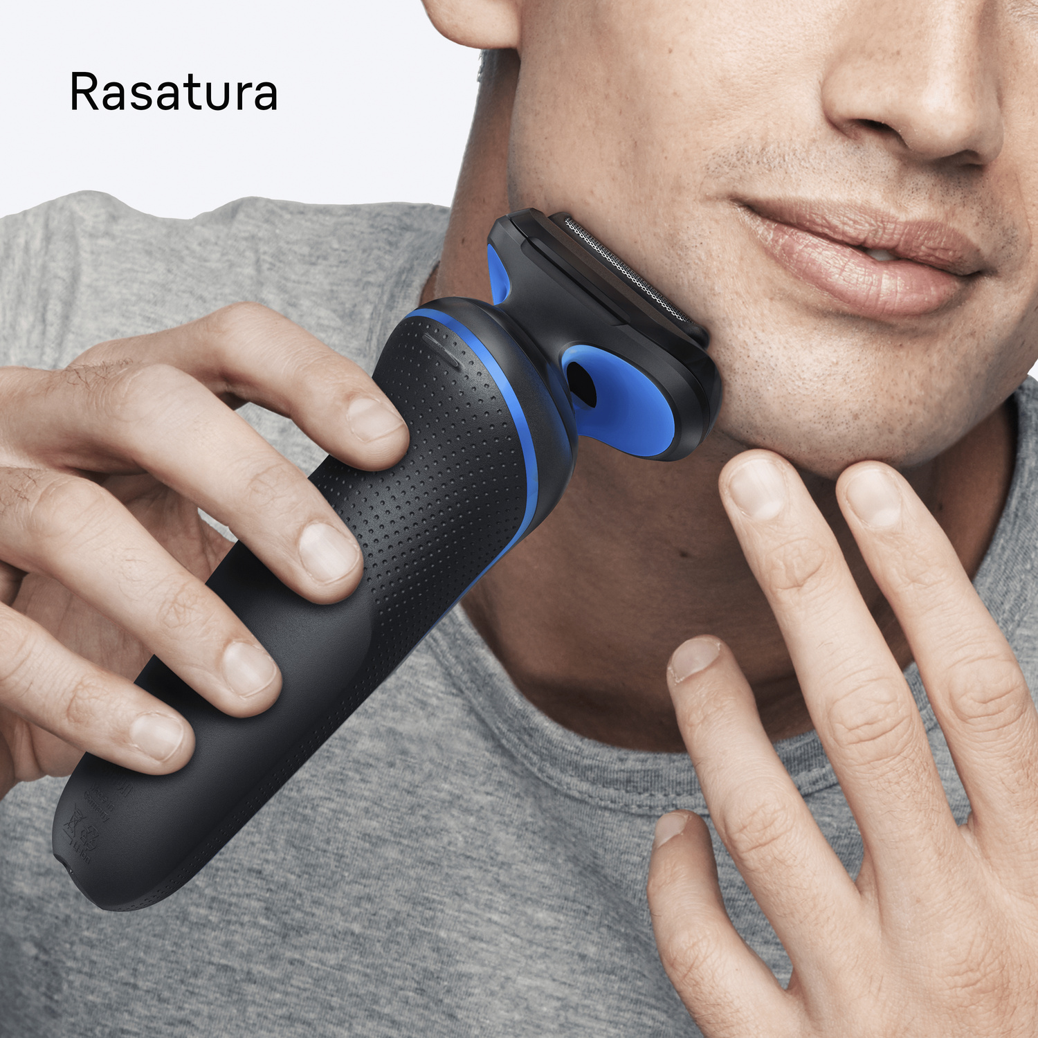 Un uomo in camicia grigia si rade il viso con un rasoio nero e blu.