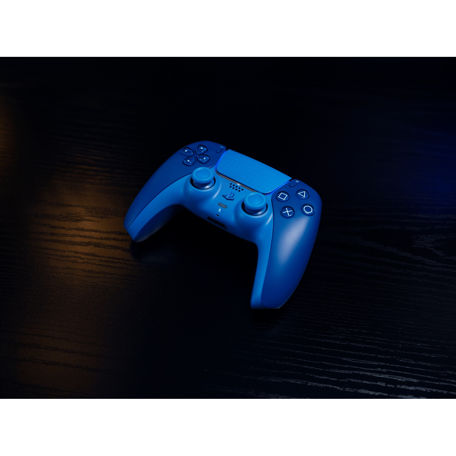 A blue PlayStation 5 controller rests on a dark wooden surface.