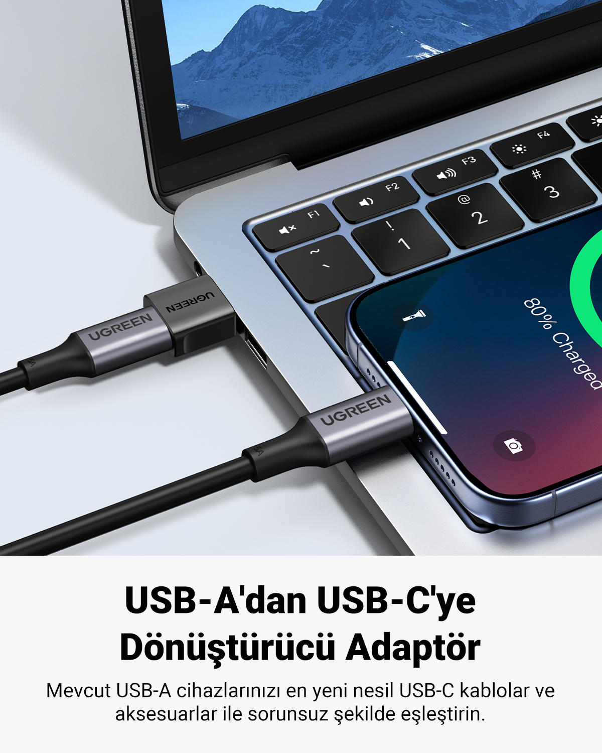 Bir dizüstü bilgisayara takılı Ugreen USB-A - USB-C adaptörü ve yanında bir akıllı telefon.