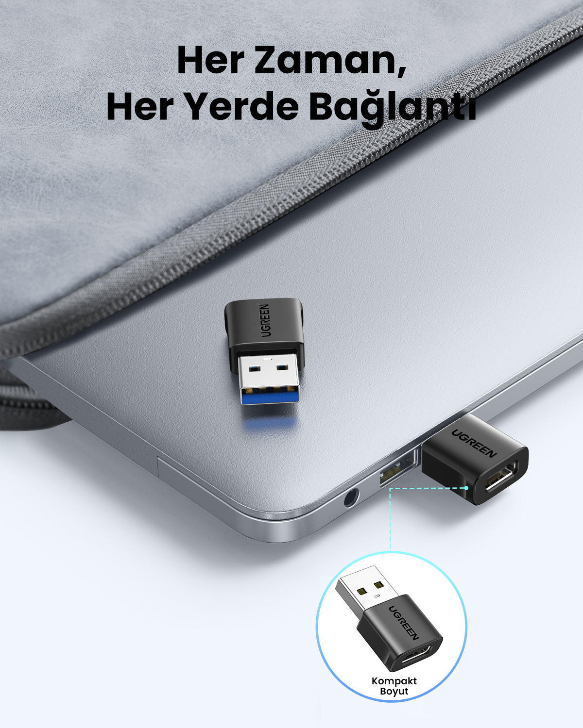 Siyah bir Ugreen USB adaptörü, dizüstü bilgisayar kılıfının yanındaki gümüş rengi bir bilgisayara takılı.