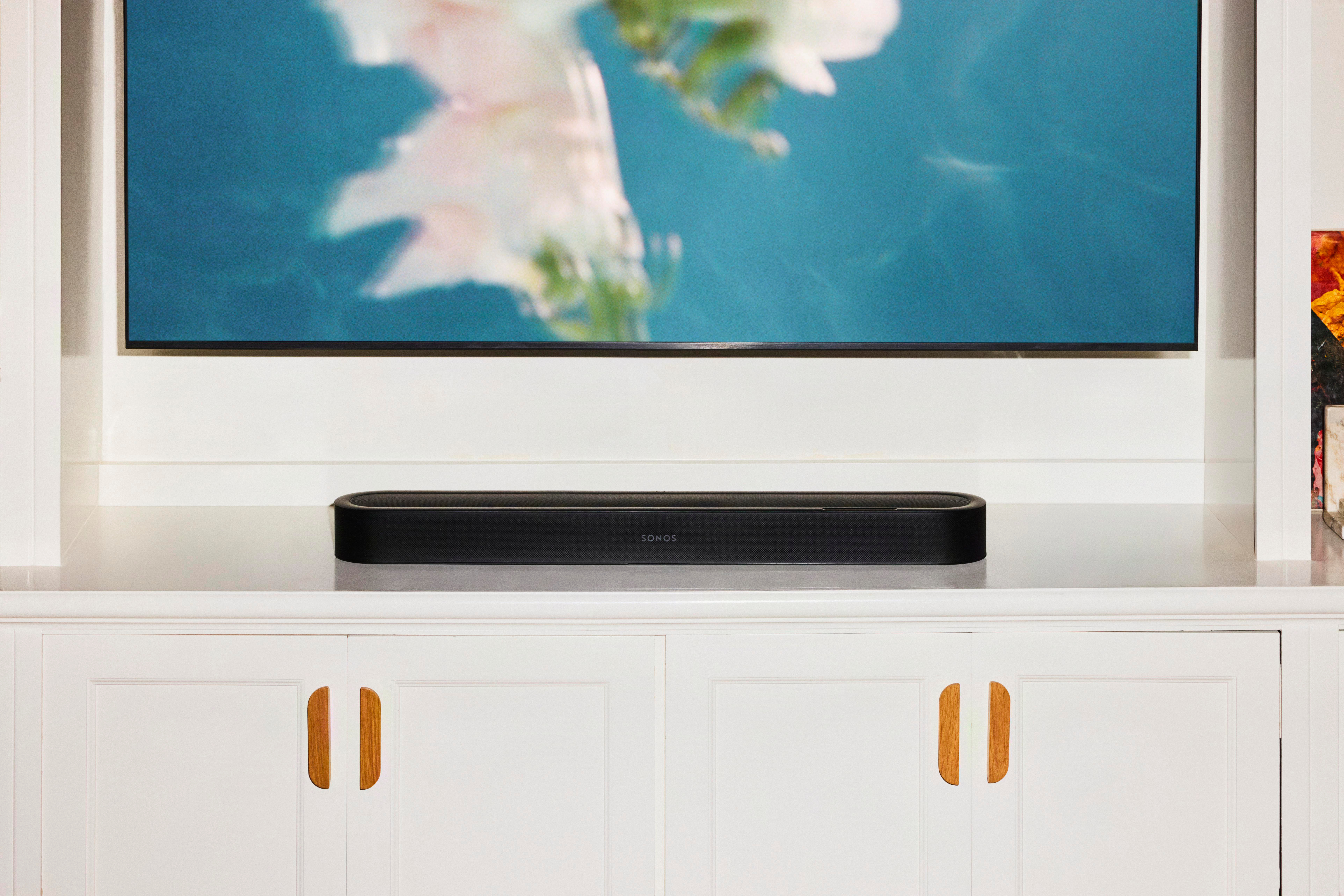 Eine schwarze Sonos Soundbar steht auf einer weißen Kommode unter einem Fernseher.